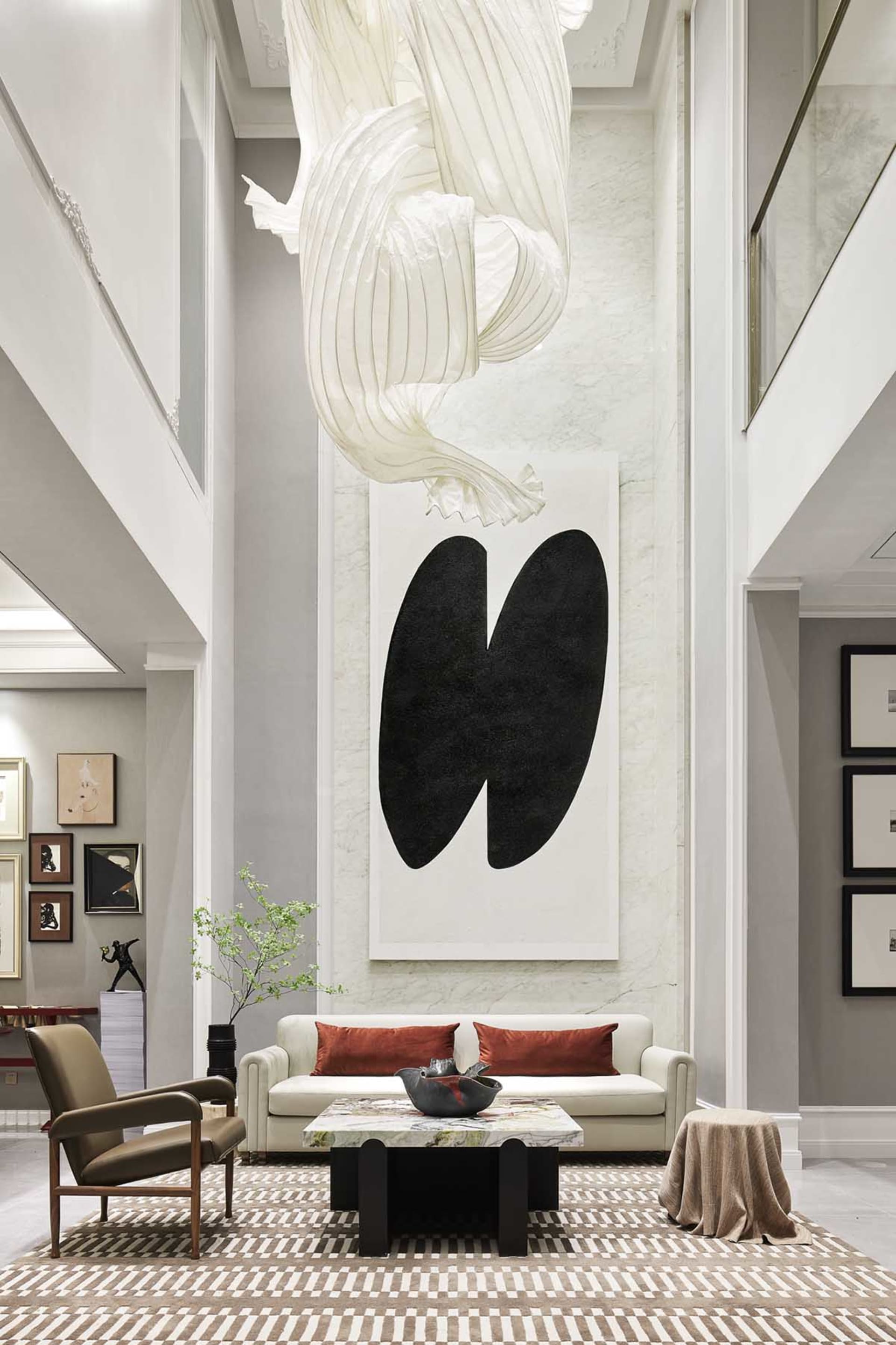 A modern white marble lobby with a white fabric sculpture and black abstract art hanging from the ceiling, white leather couc