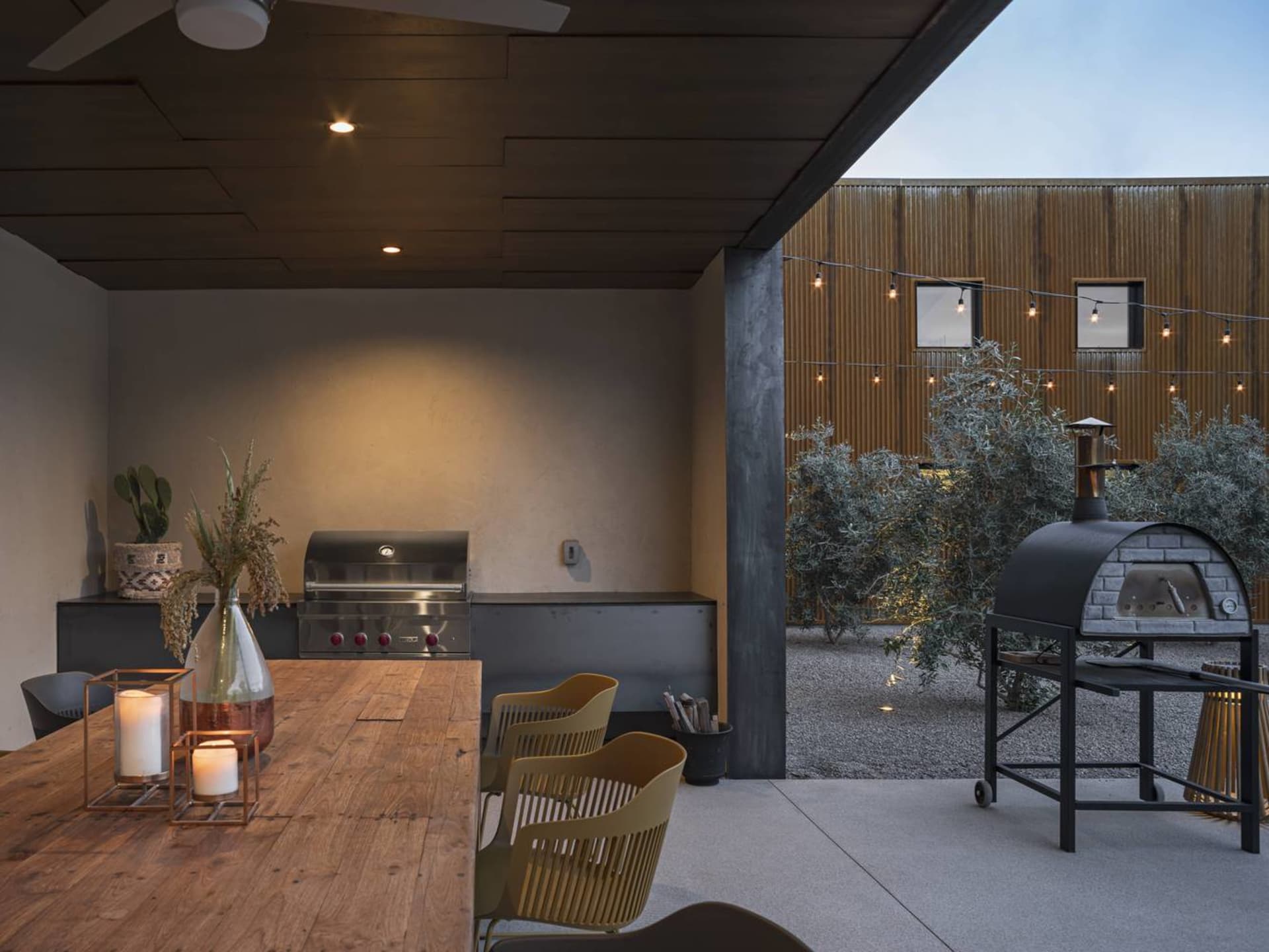 Outdoor kitchen with metal appliances, concrete countertop, and string lights.
