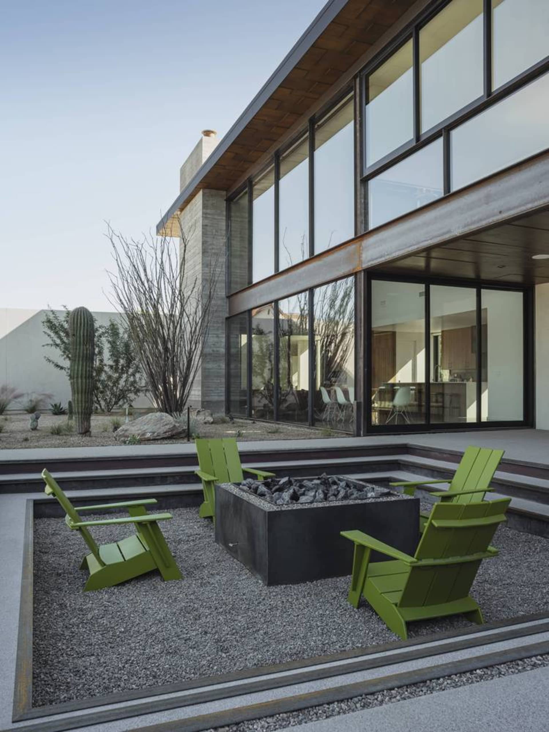 Modern metal patio furniture set with a fire pit in a gravel area.
