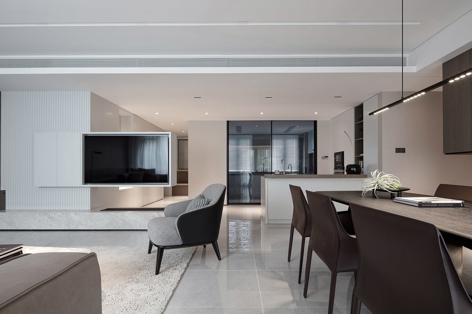 Modern minimalist living room, dining area, and kitchen integrated into a single space with sleek, clean lines and a neutral