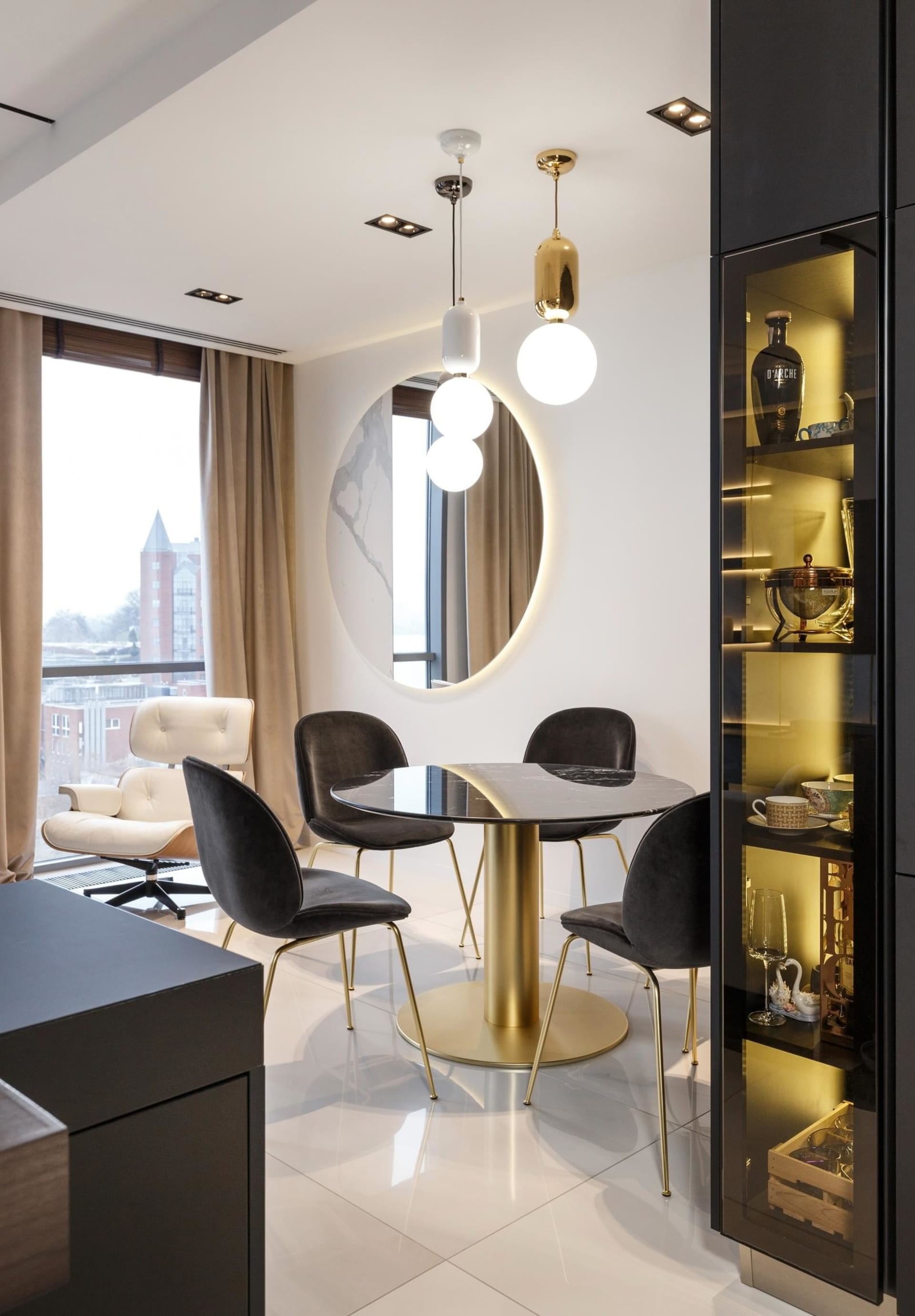 Modern, sleek, white kitchen and dining area featuring black marble table and gold-brass chairs, illuminated by pendant light