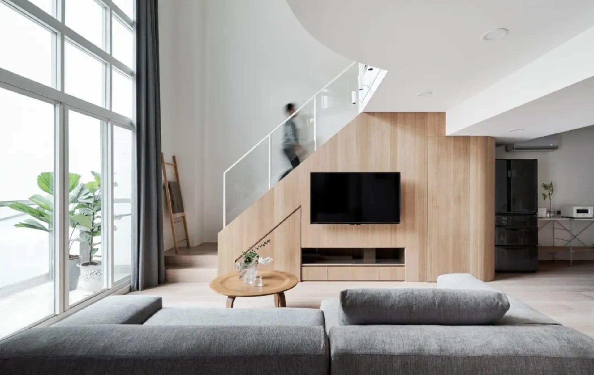A minimalist living room with a glass staircase, wooden sofa, and floor-to-ceiling windows
