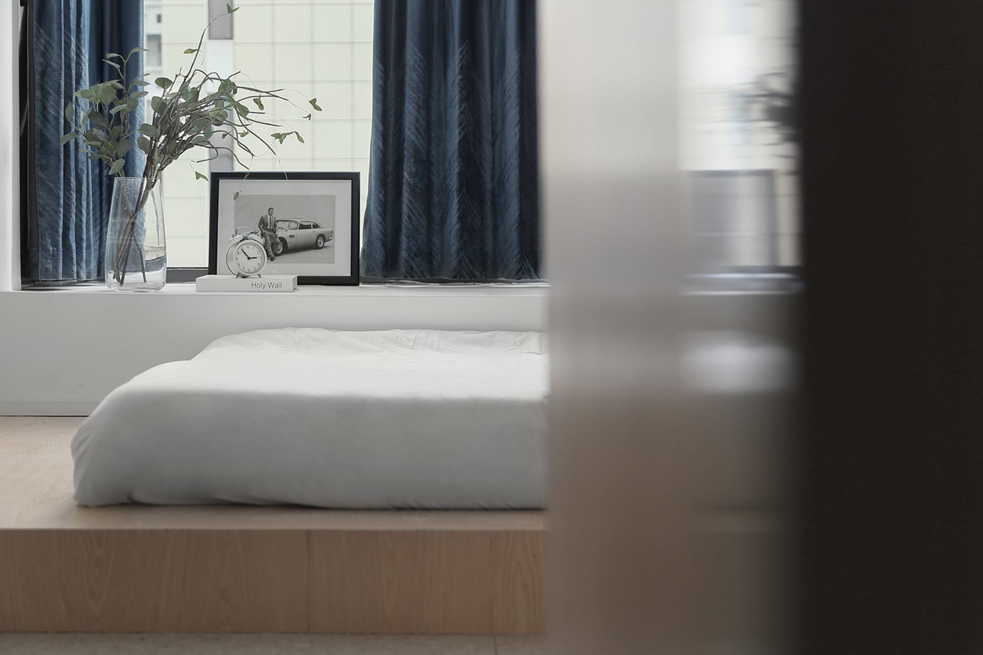 Minimalist bedroom with a wood frame bed, white bedding, and blue curtains.
