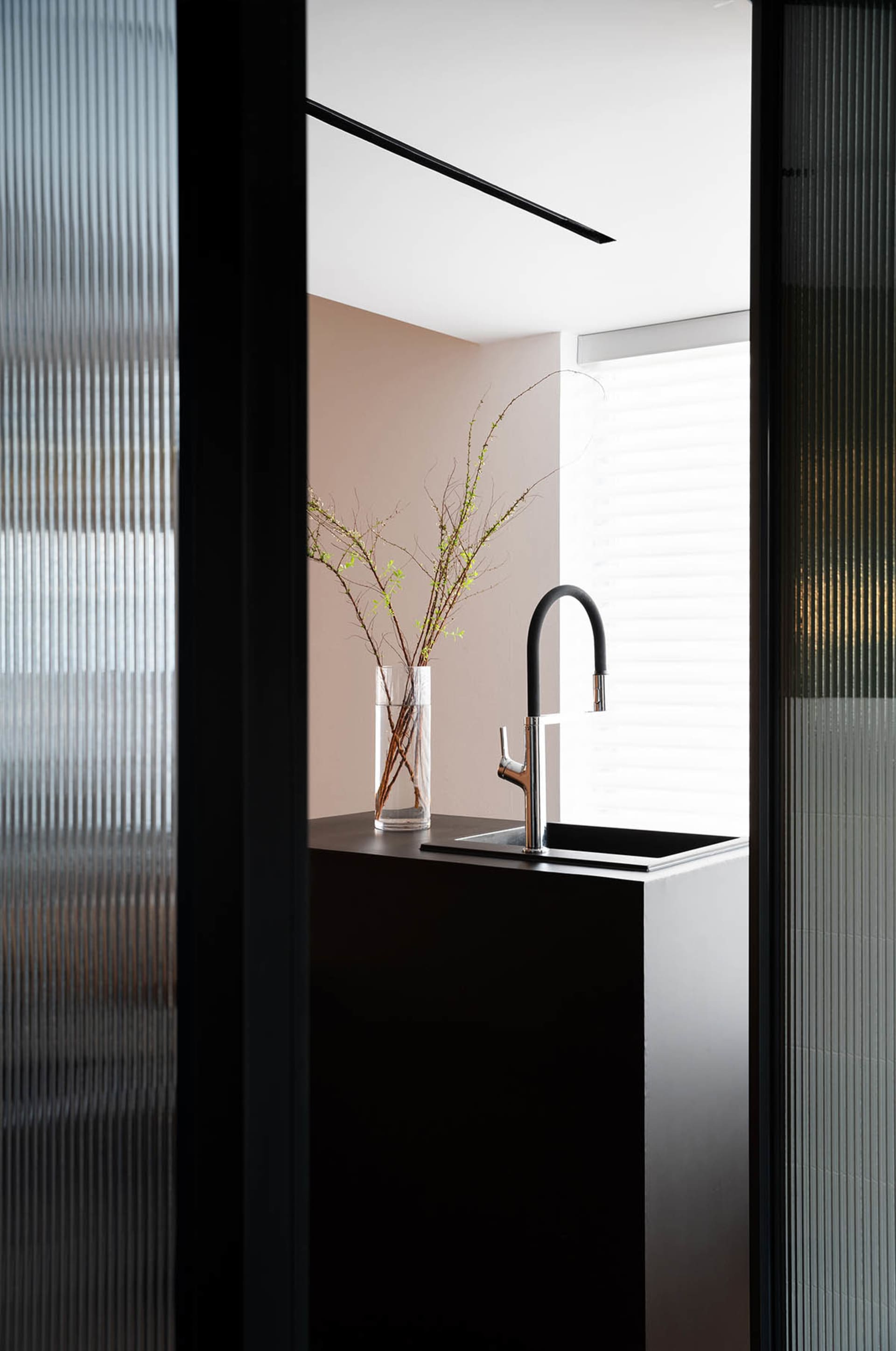 A modern minimalist kitchen with a transparent window featuring a vase with branches, a sleek faucet, and a minimalist aesthe