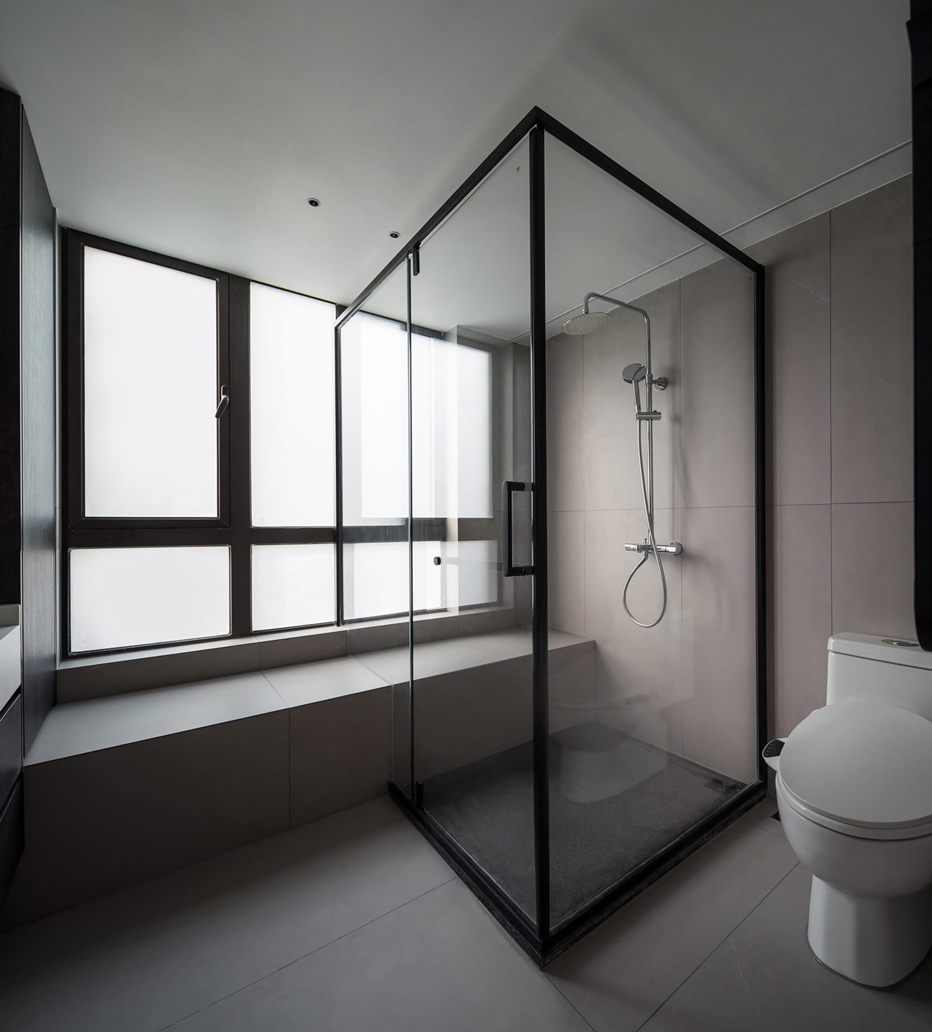 A minimalist modern bathroom with glass shower enclosure, white tiles, and a window seat.