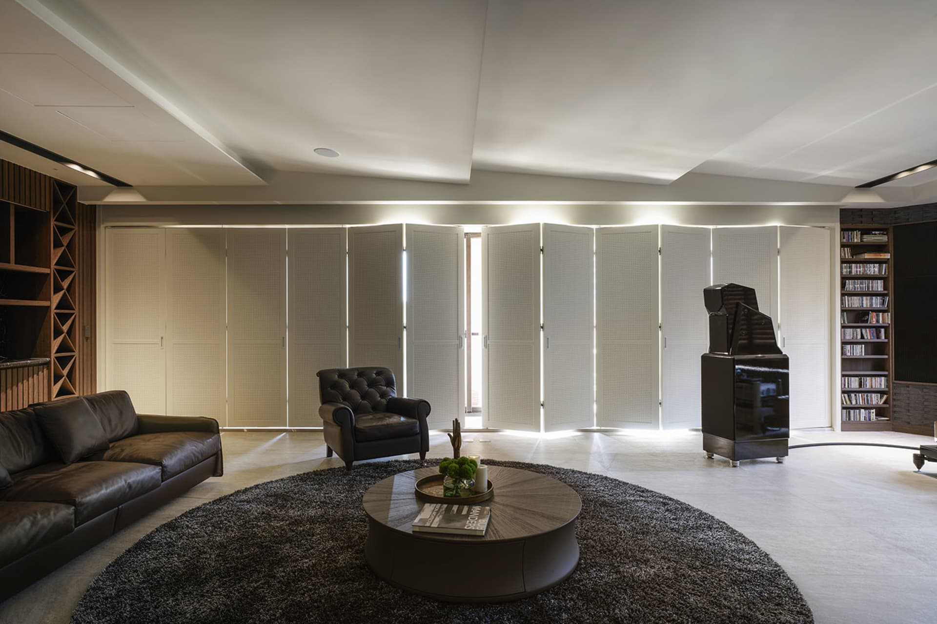 A modern living room with a white perforated panel, black leather furniture, and a round coffee table.