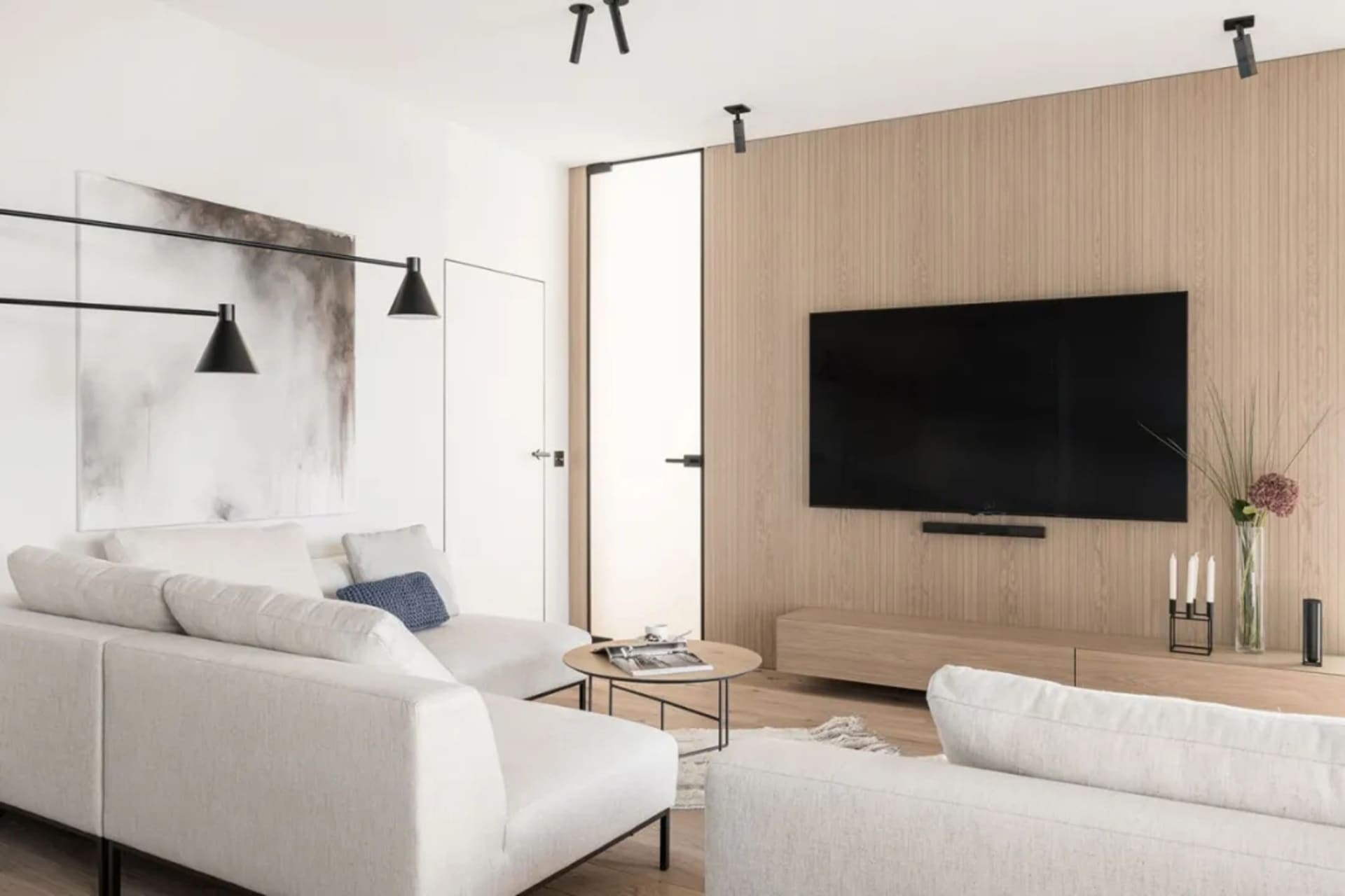Modern minimalist living room with white and grey furniture, a wooden wall, and a large flat-screen TV.