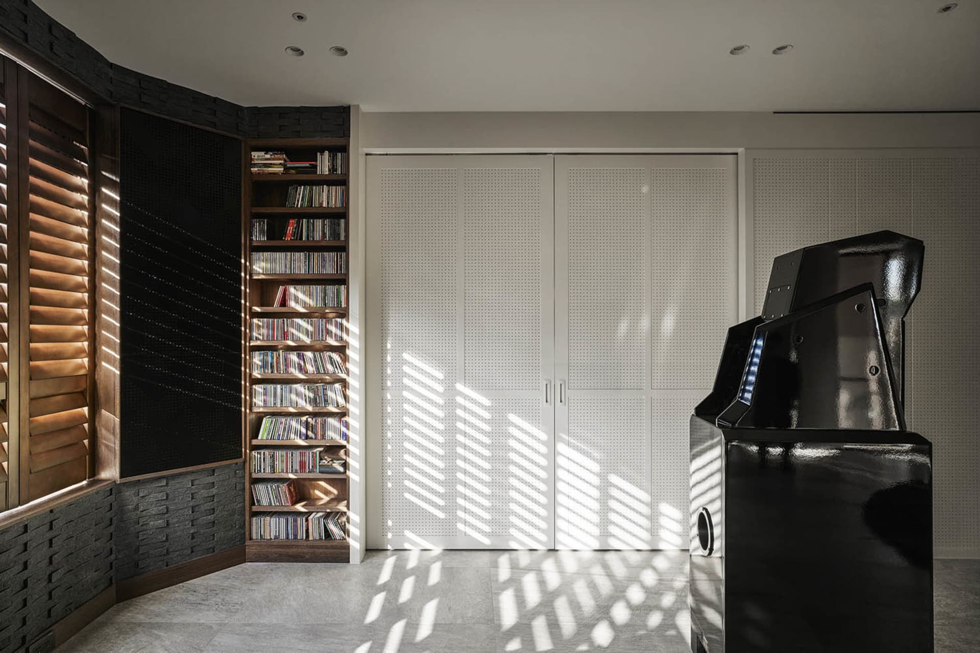A modern living room featuring a bookshelf filled with books and a large black gaming cabinet, with light streaming through t