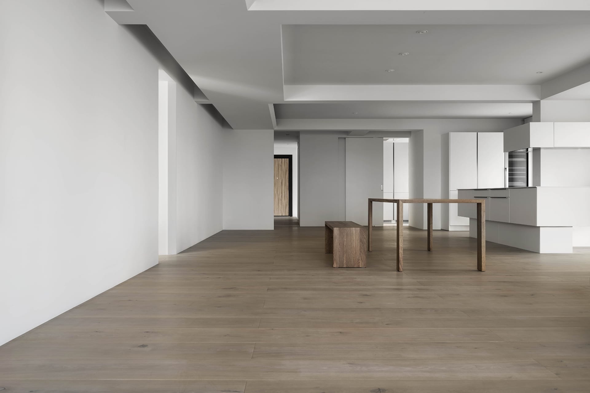 A modern minimalist kitchen featuring wooden furniture and white surfaces.