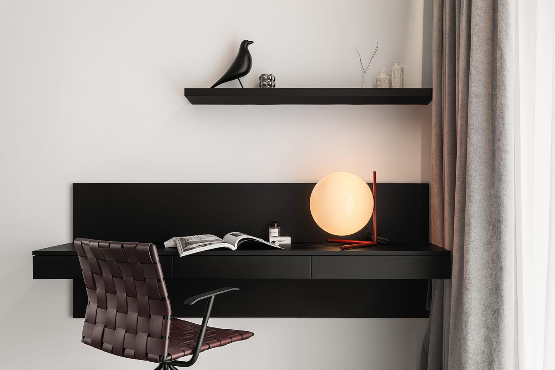 A modern black wood home office setup with a leather chair, minimalist desk, and green plant.