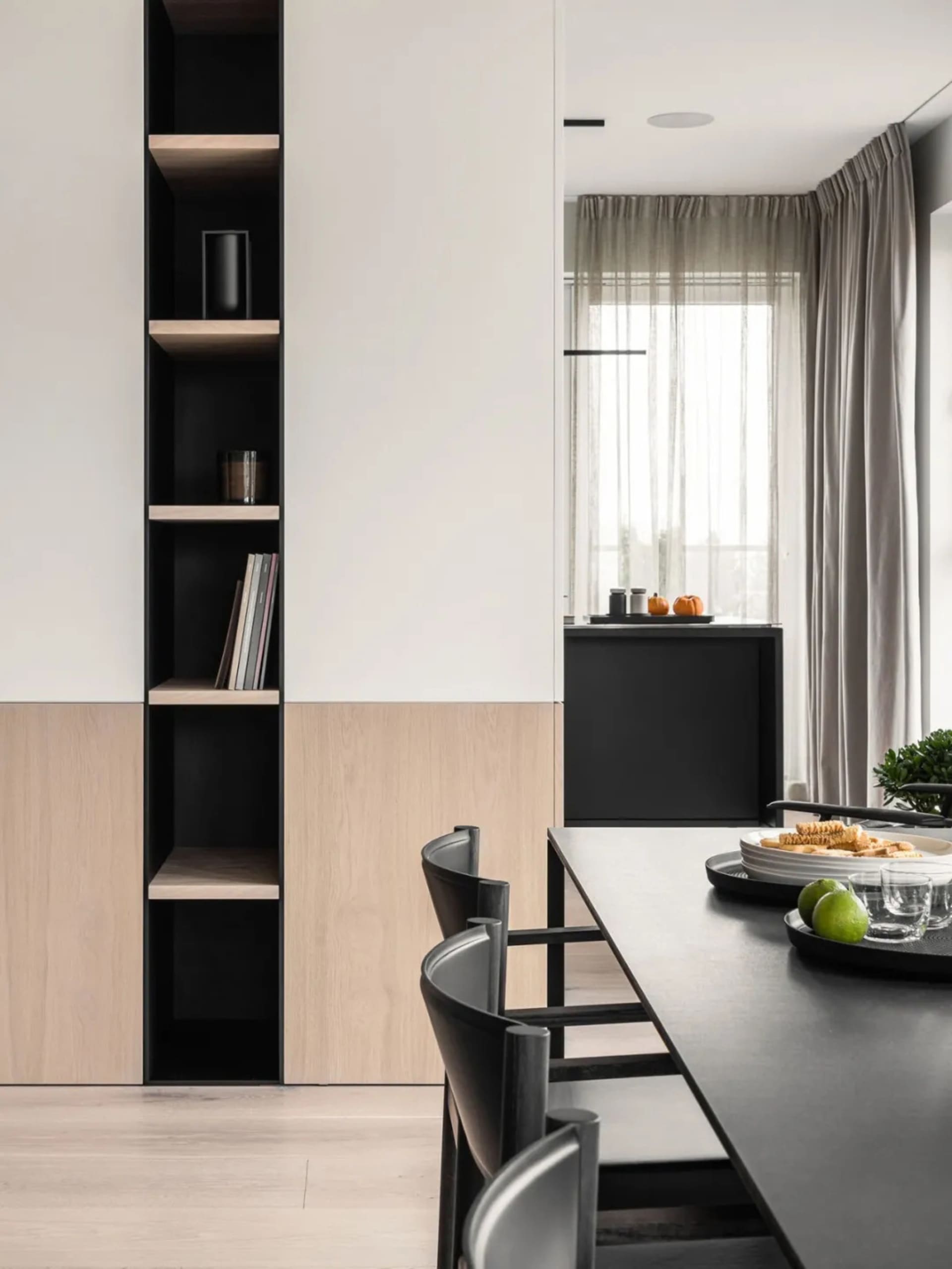 A modern dining room featuring minimalist furniture, sleek black and light wood finishes, and a long black dining table surro
