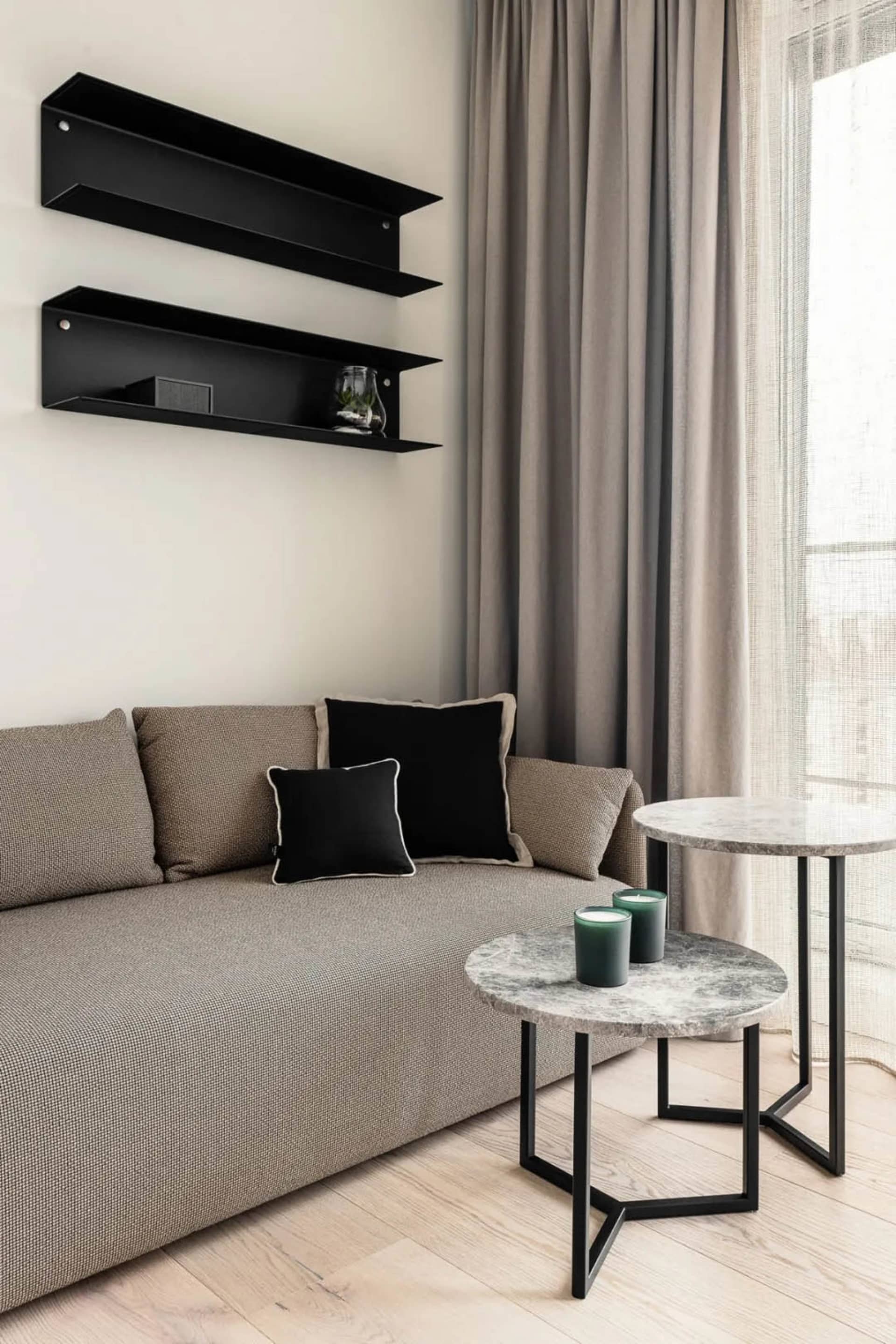 A modern living room featuring a grey couch adorned with black cushions and black floating shelves on the wall.