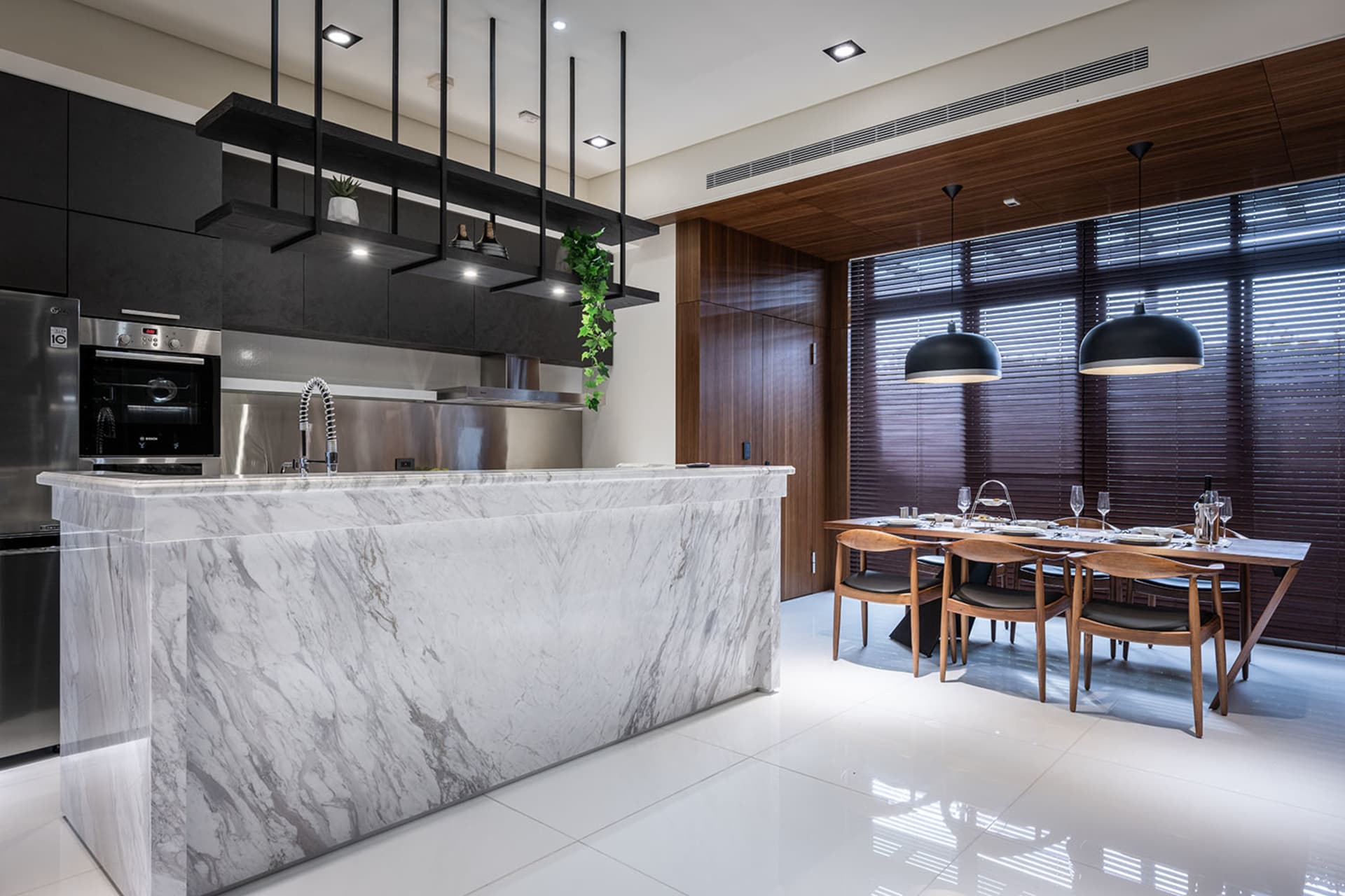 A modern residential living space featuring marble countertops, wooden dining chairs, and stainless steel appliances.