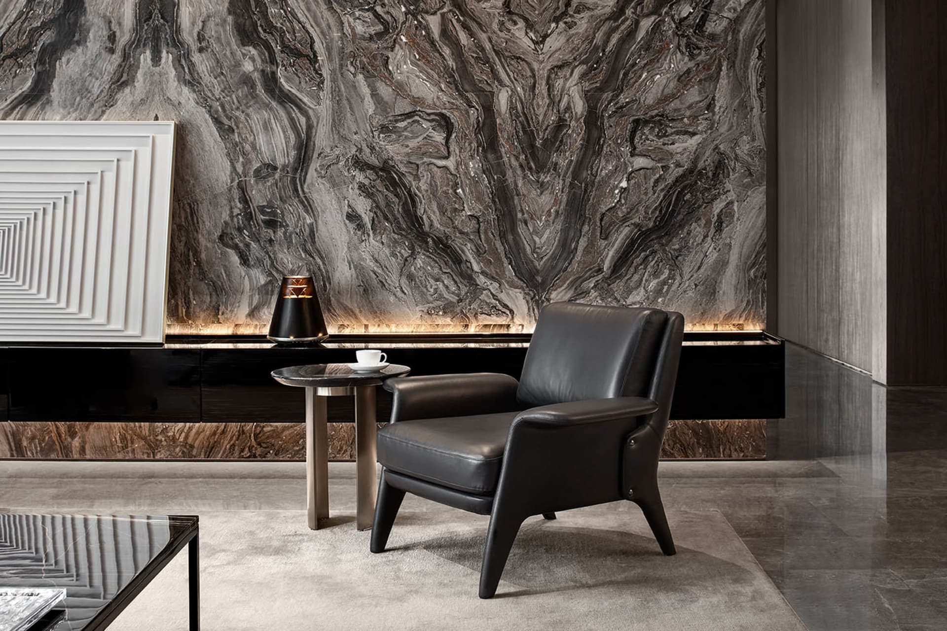 Modern living room with a grey leather armchair, marble side table, and a coffee table with a geometric frame. The wall featu