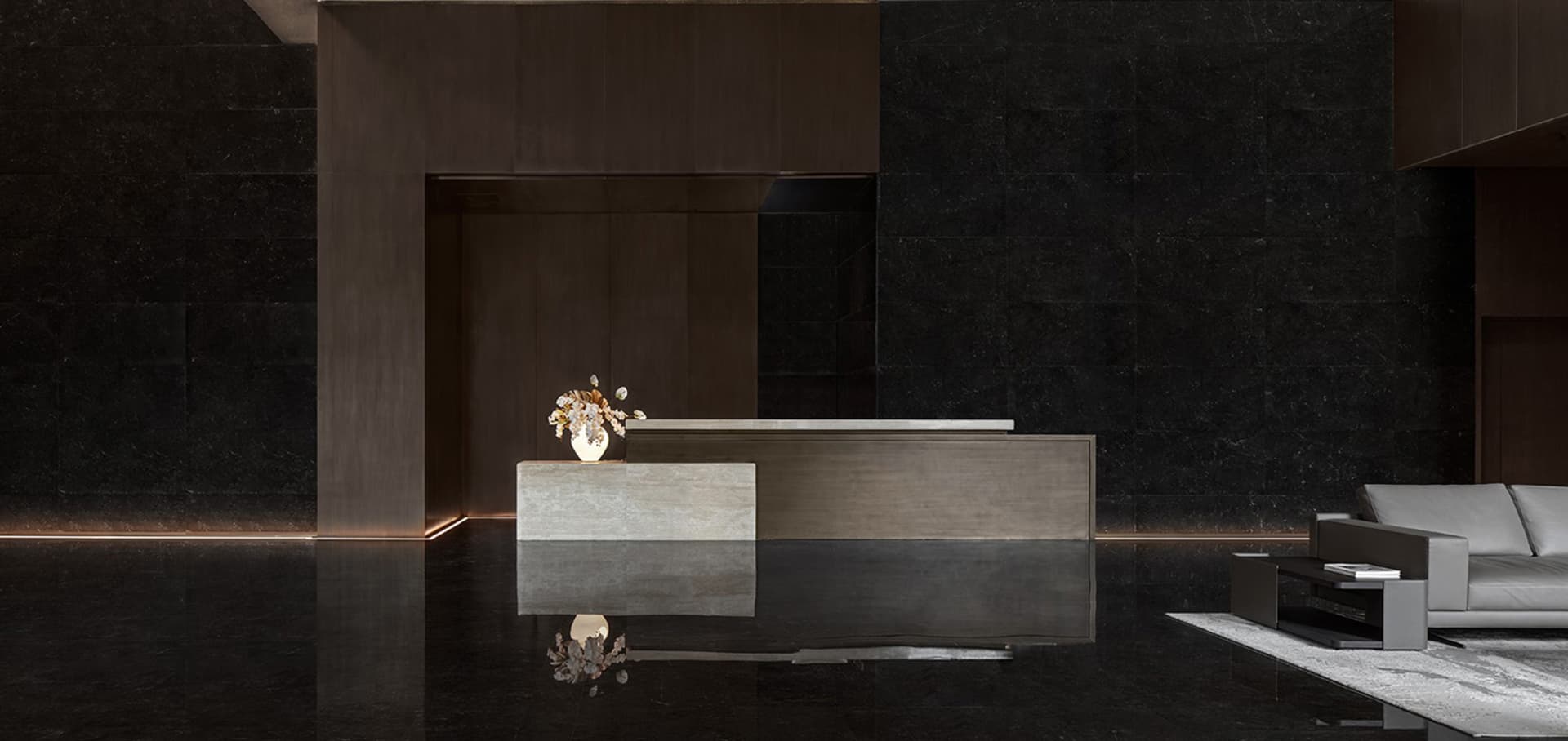 A modern lobby with a concrete reception desk, white vase with flowers, and a grey sofa on a white rug.