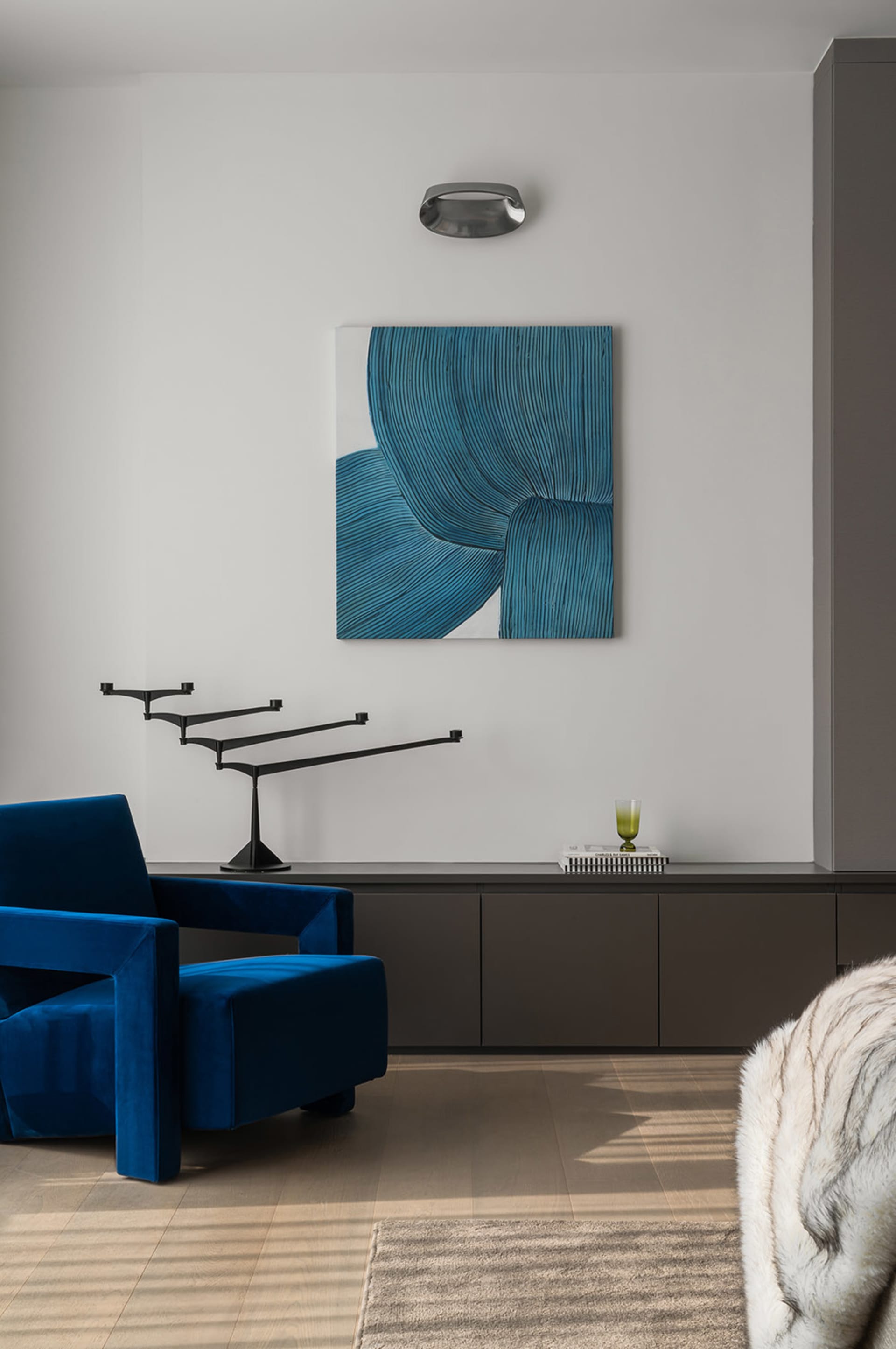 Modern living room featuring a blue velvet couch, abstract art, and sleek, dark wooden cabinets.