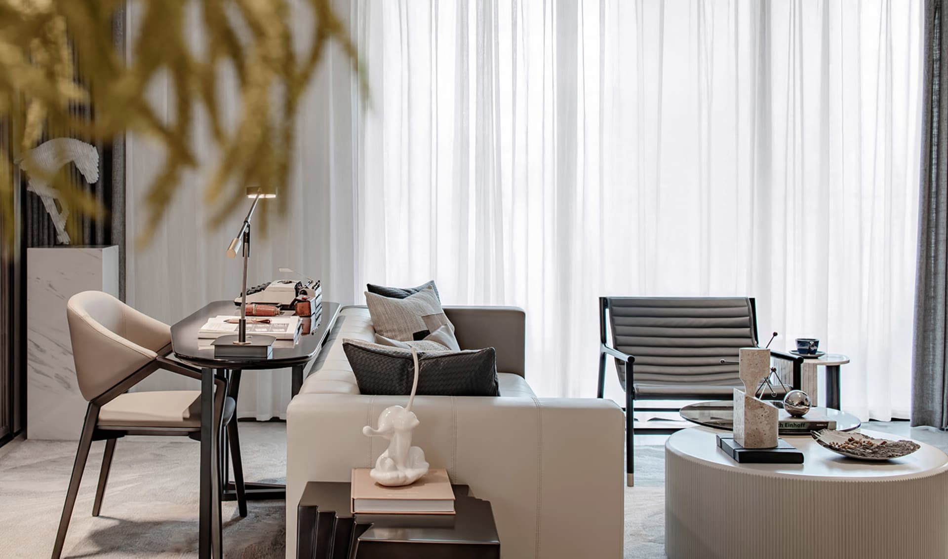 A minimalist living room featuring a cream-colored sofa, a round coffee table, and a white desk with a black and white table