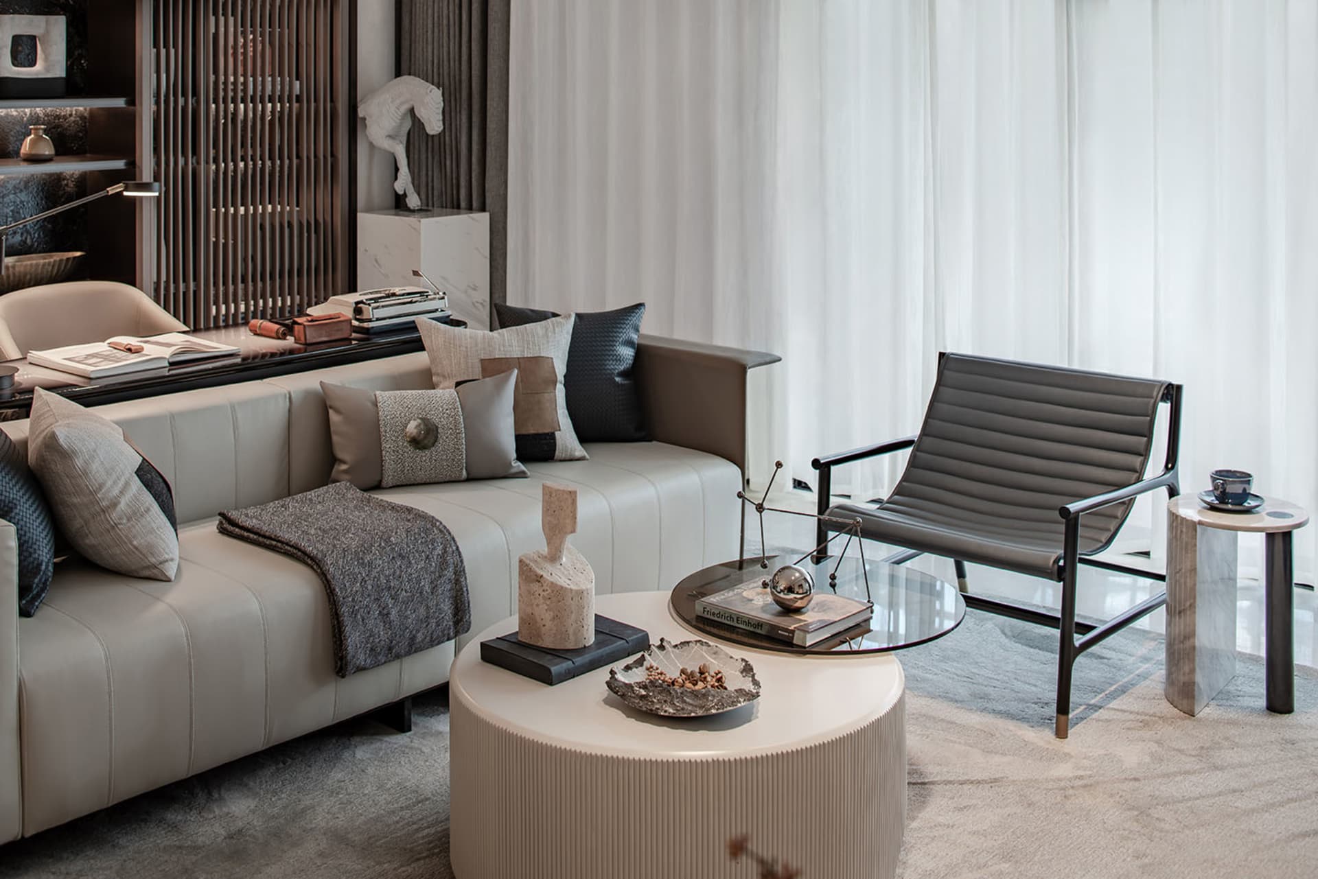 A modern living room with neutral-toned furniture, including a white sofa with patterned pillows, a glass coffee table, and a