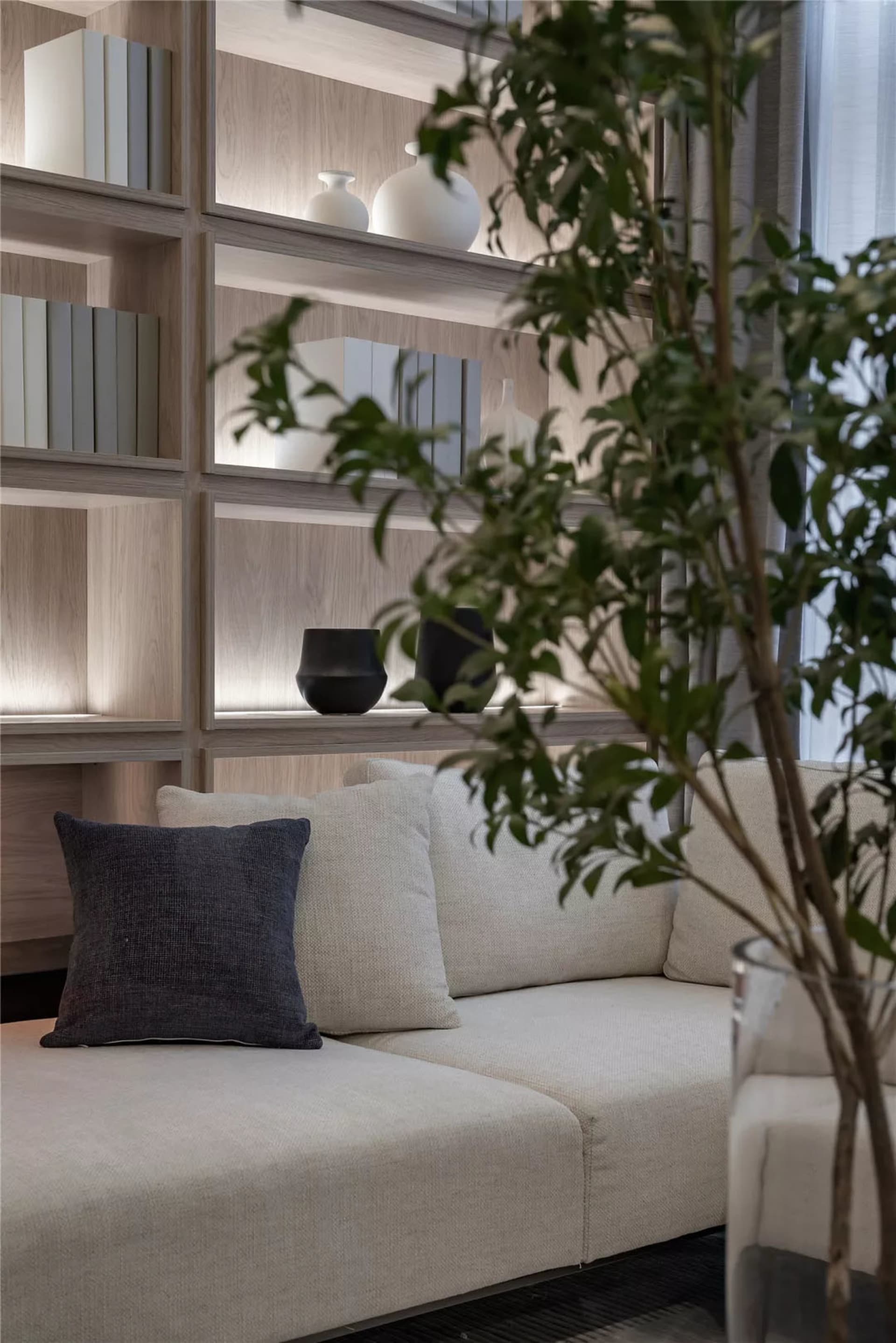 A modern living room featuring a sectional couch with blue and white cushions and a wooden bookshelf filled with books and de