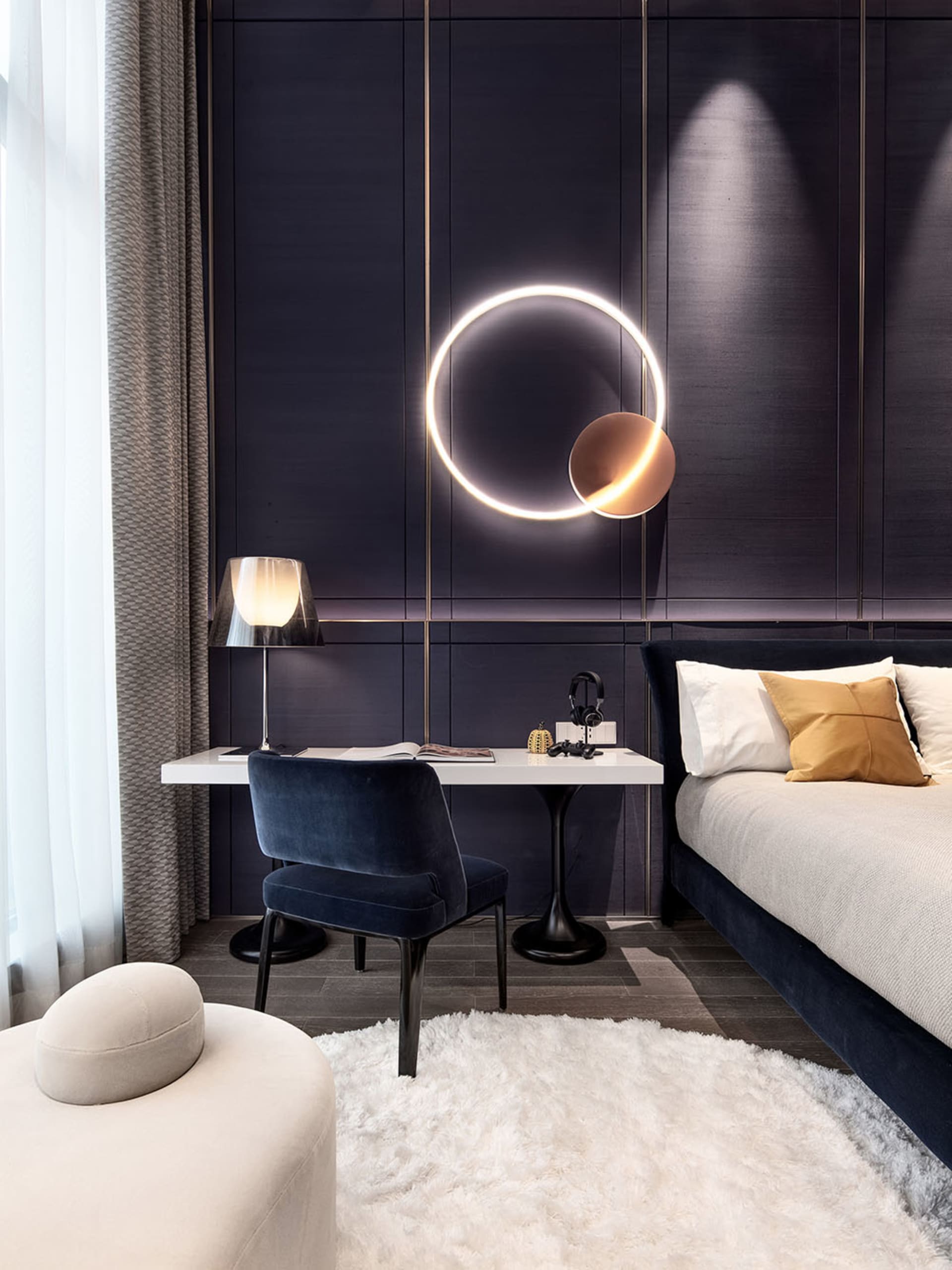 A modern minimalist bedroom with black walls and a white desk, featuring a white fur rug and a circular light fixture.