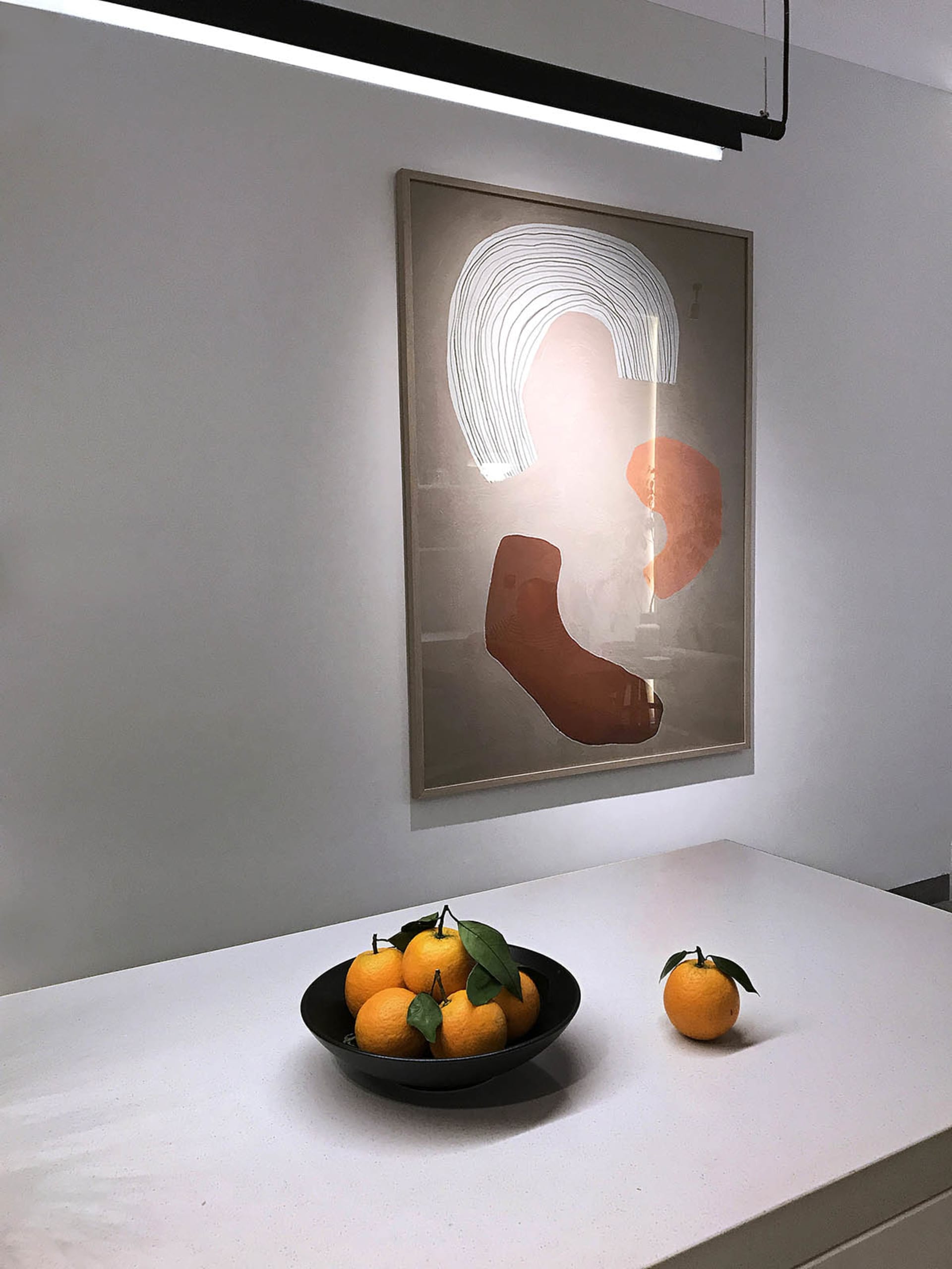 A modern minimalist kitchen with abstract art, oranges, and white countertops.