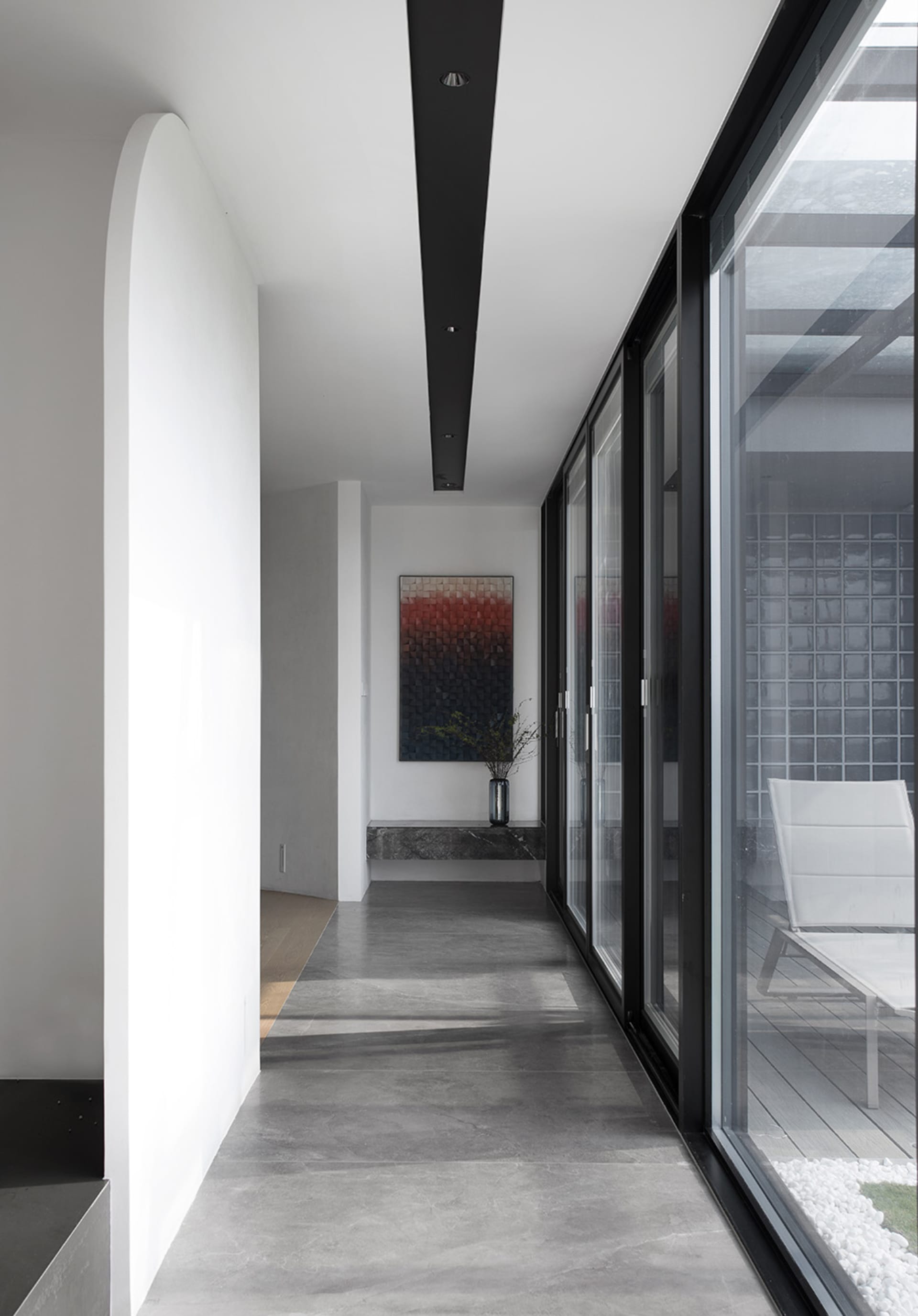 A minimalist interior design featuring a concrete pathway with a view of an outdoor seating area.