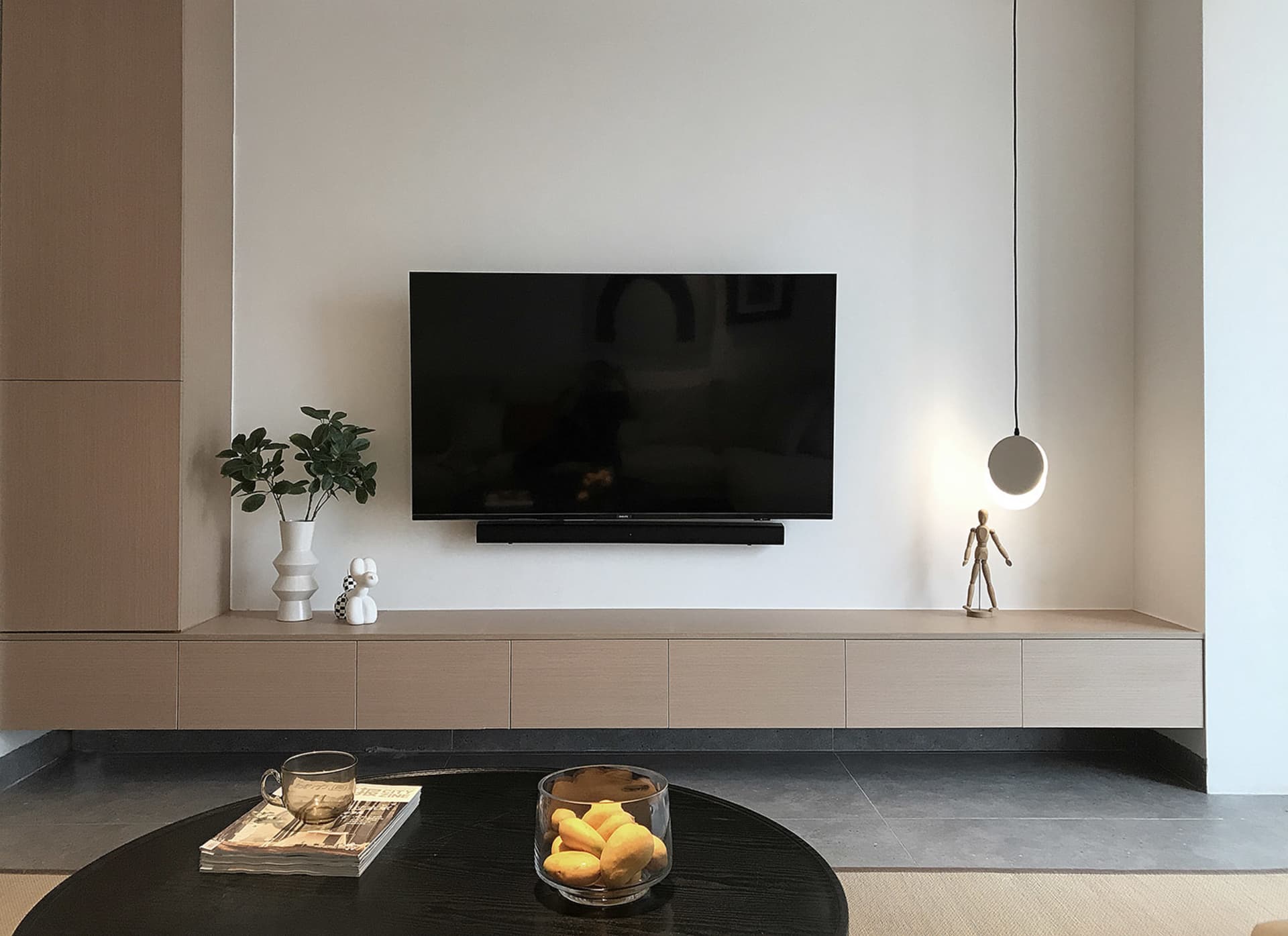 一間現代客廳,擺放木質家具、圓形黑色咖啡桌,以及壁掛式平面電視。