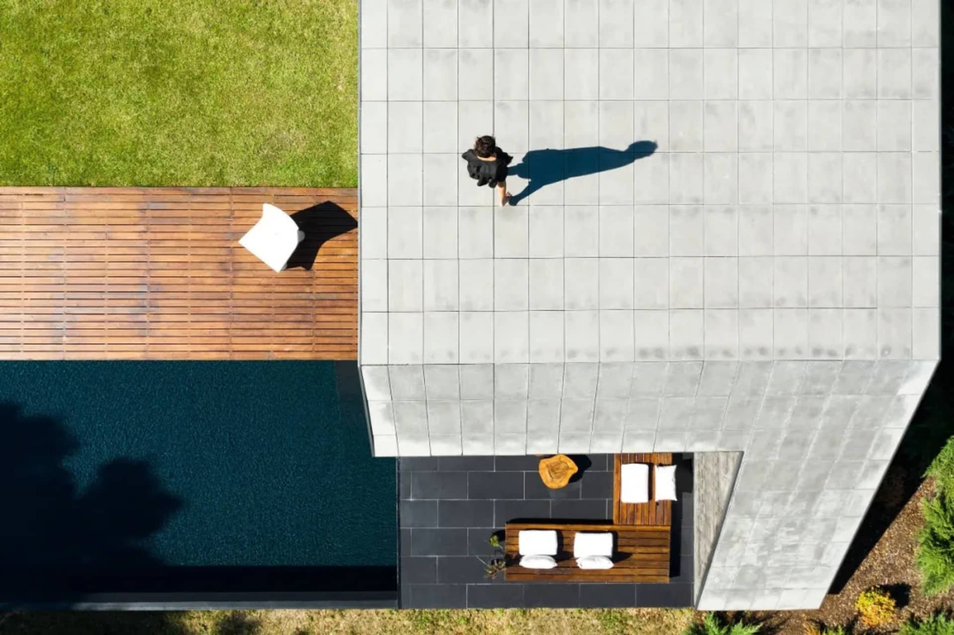A modern, minimalist exterior features concrete tiles and wooden elements. A person walks on the rooftop patio.