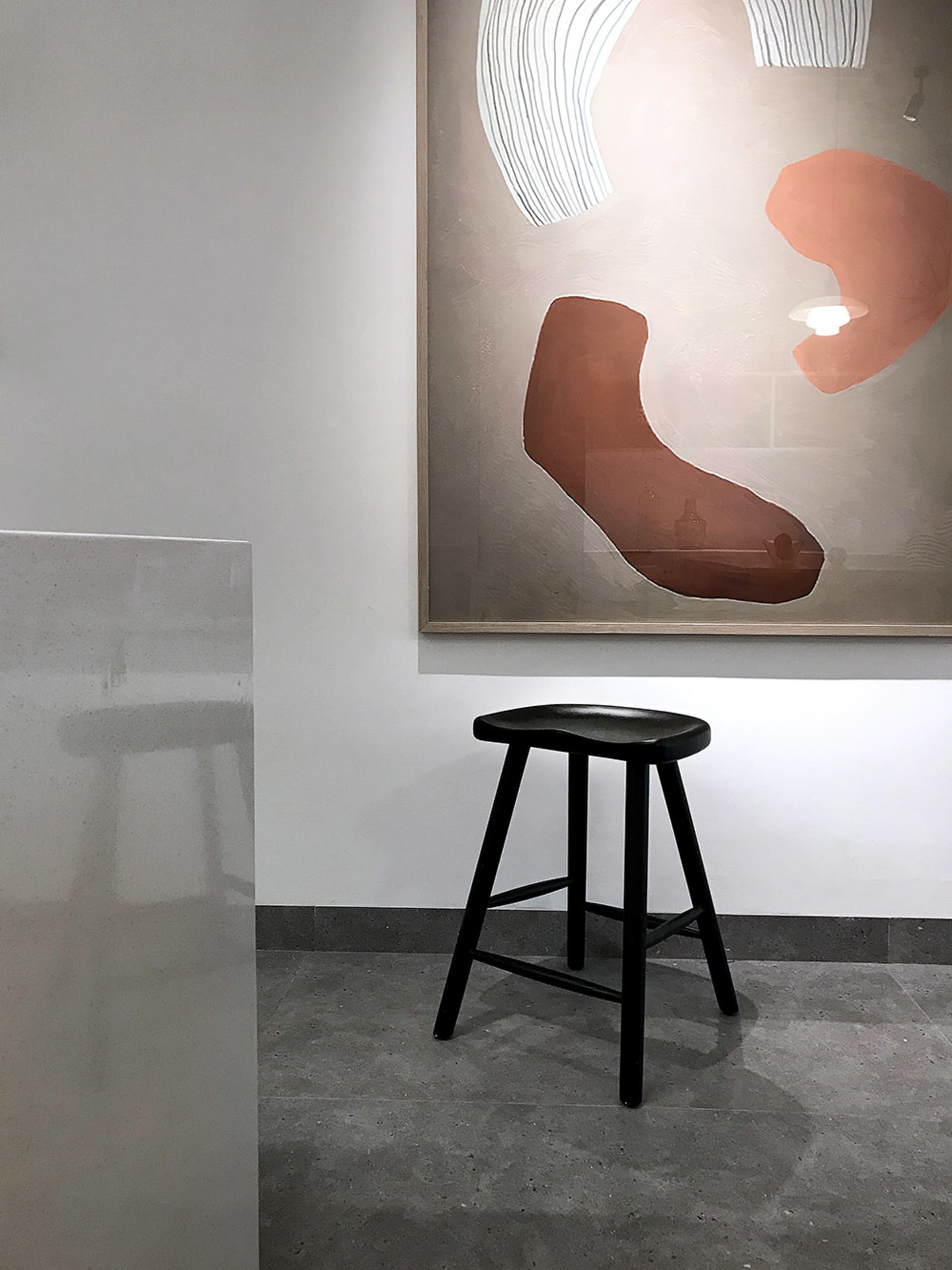 現代藝術展覽空間，黑色凳子置於混凝土地板上，牆面懸掛抽象畫作。
