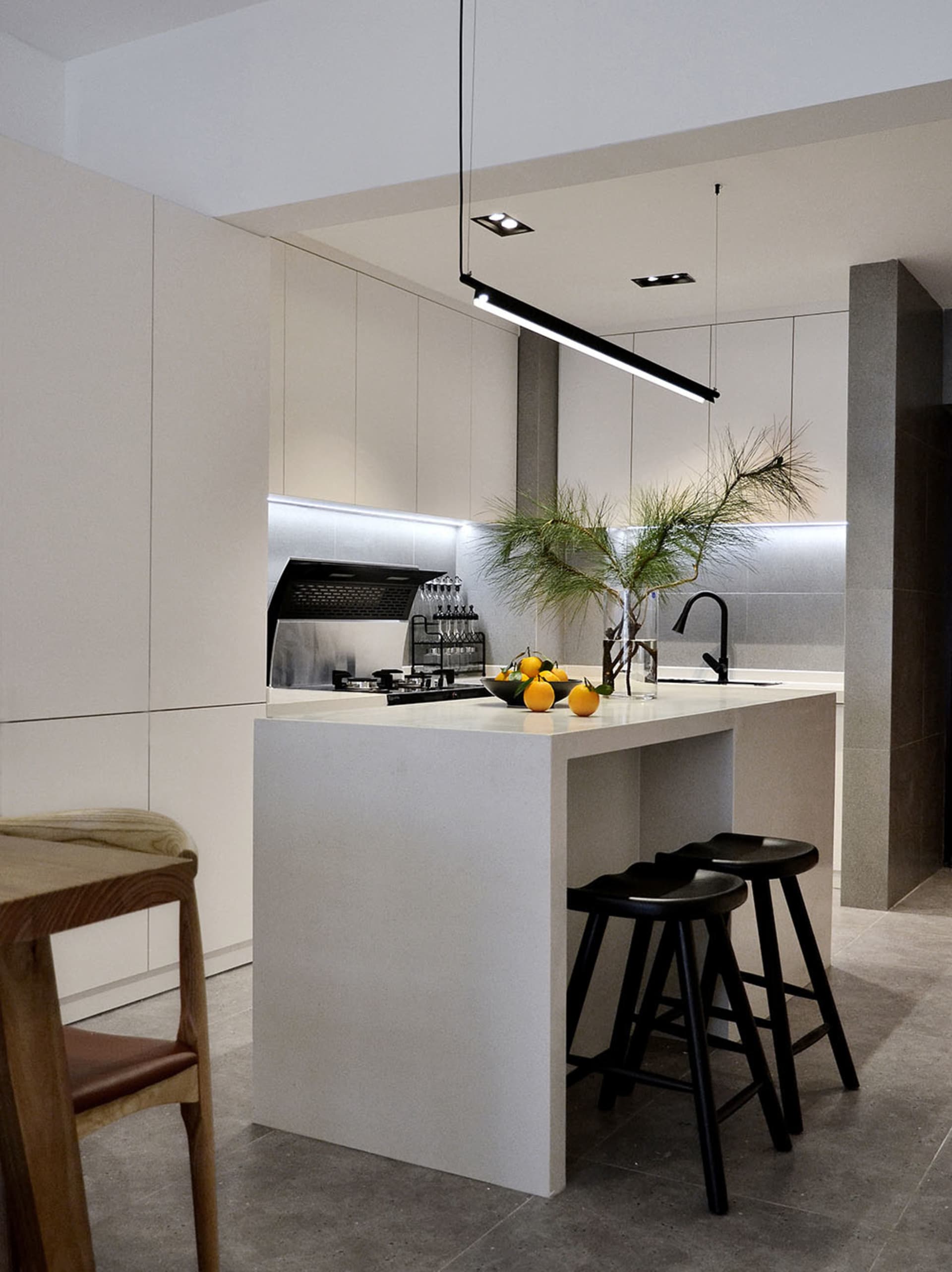 A modern minimalist residential kitchen featuring white cabinets, a white countertop, and a white island with black stools an