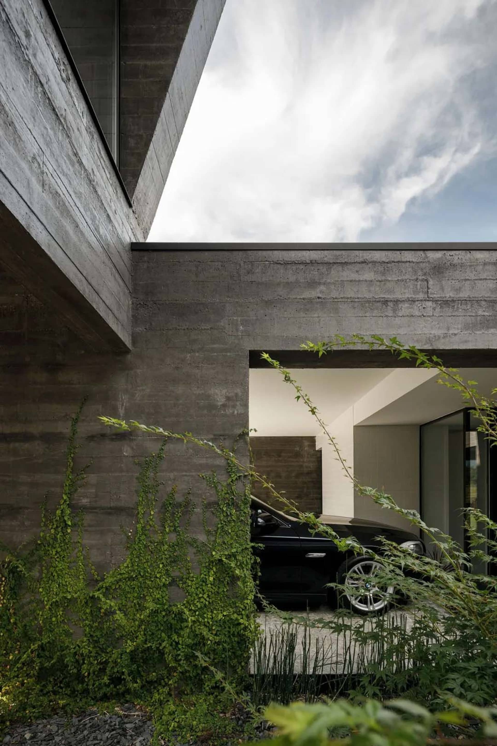 A modern residential building with a minimalist design, featuring a concrete exterior and an open-air carport.