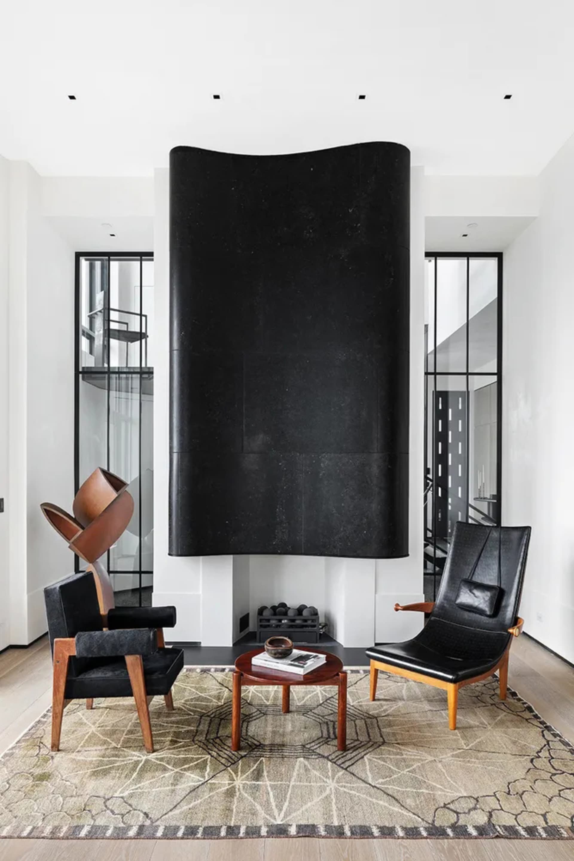 A modern living room with a black, wall-mounted fireplace, black leather armchairs, a round wooden coffee table, and a patter