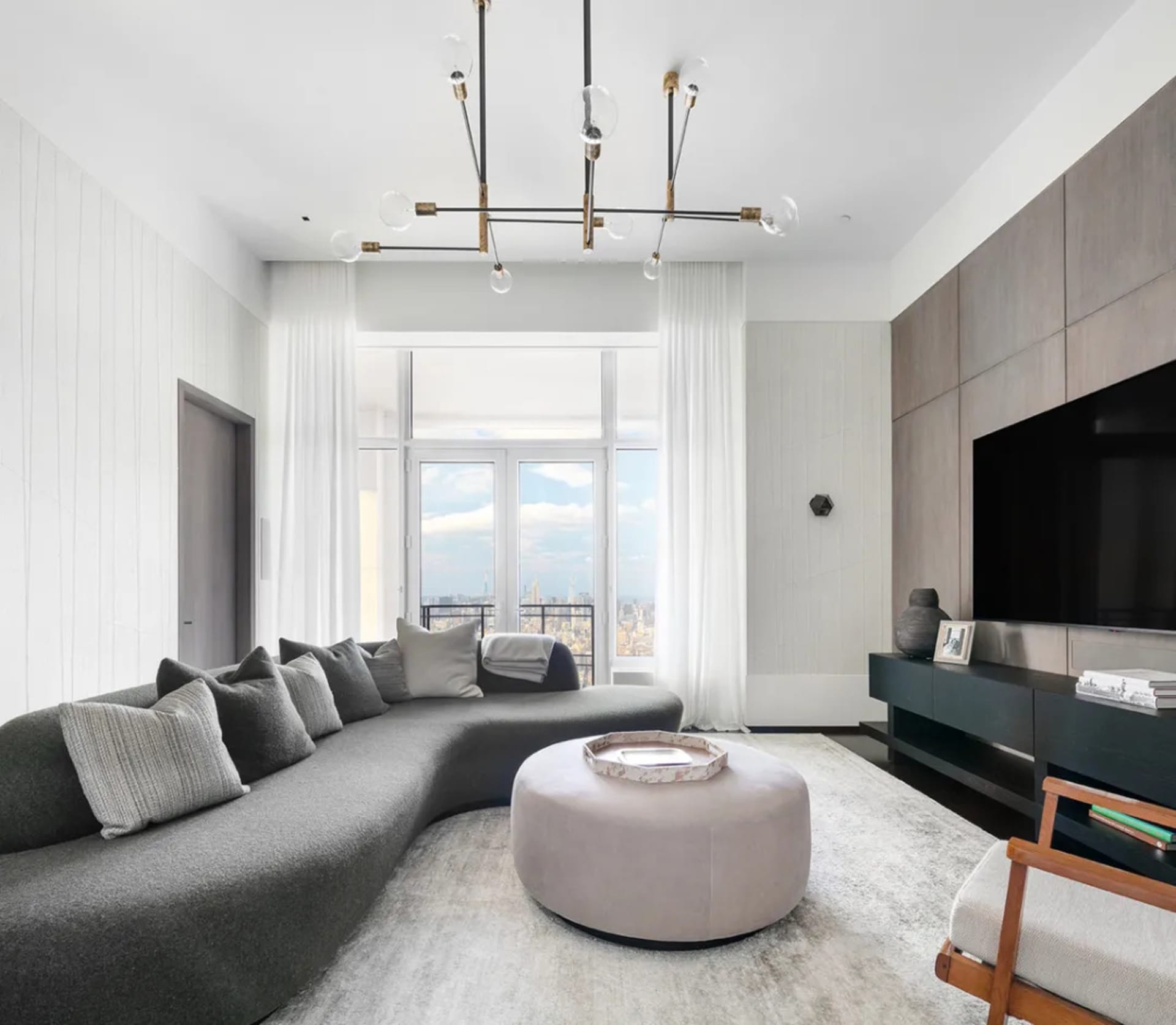 Modern living room featuring glass and wooden furniture and a large window with city skyline view.