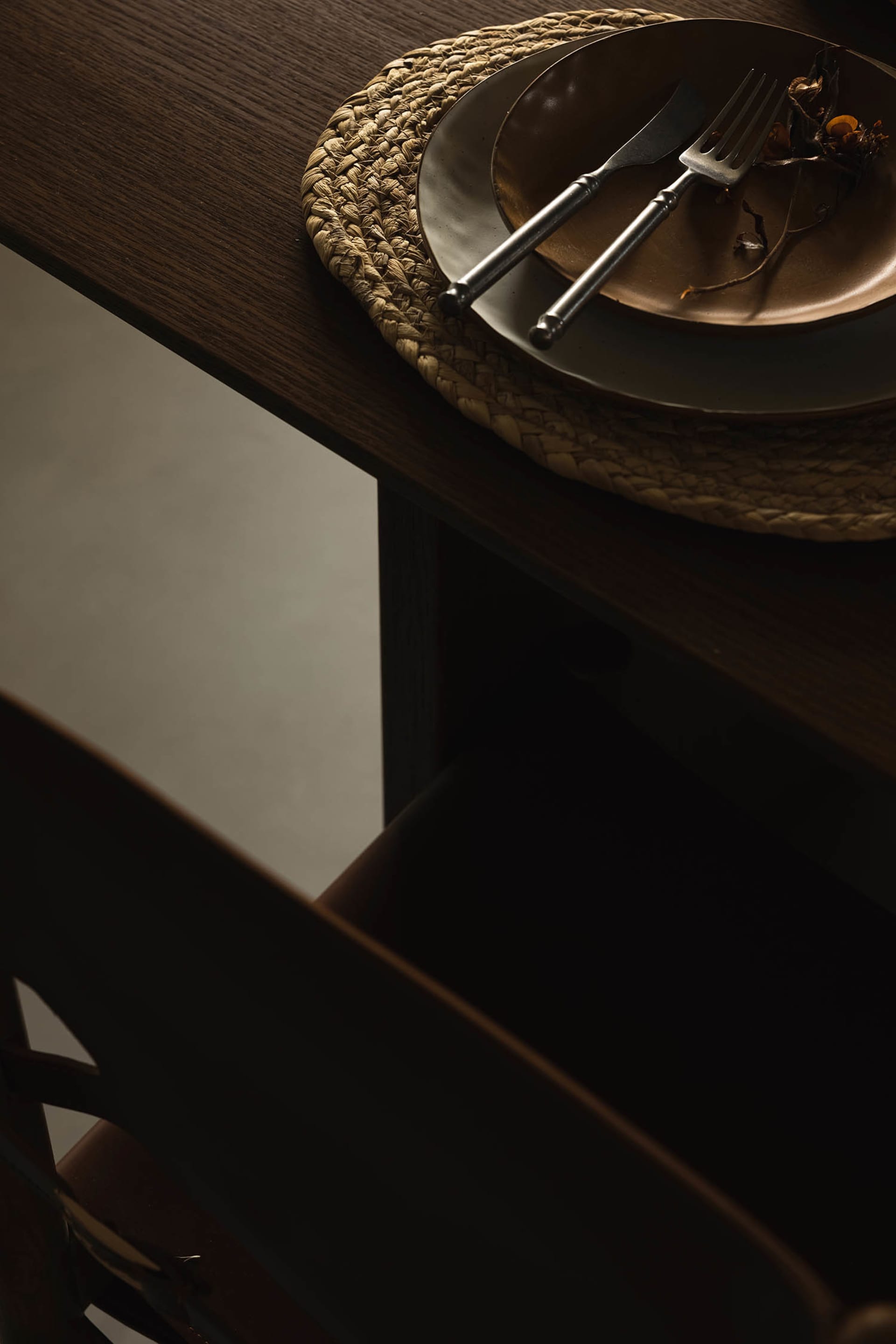 An industrial dining table setting featuring a metal plate with a knife and fork on a woven place mat.