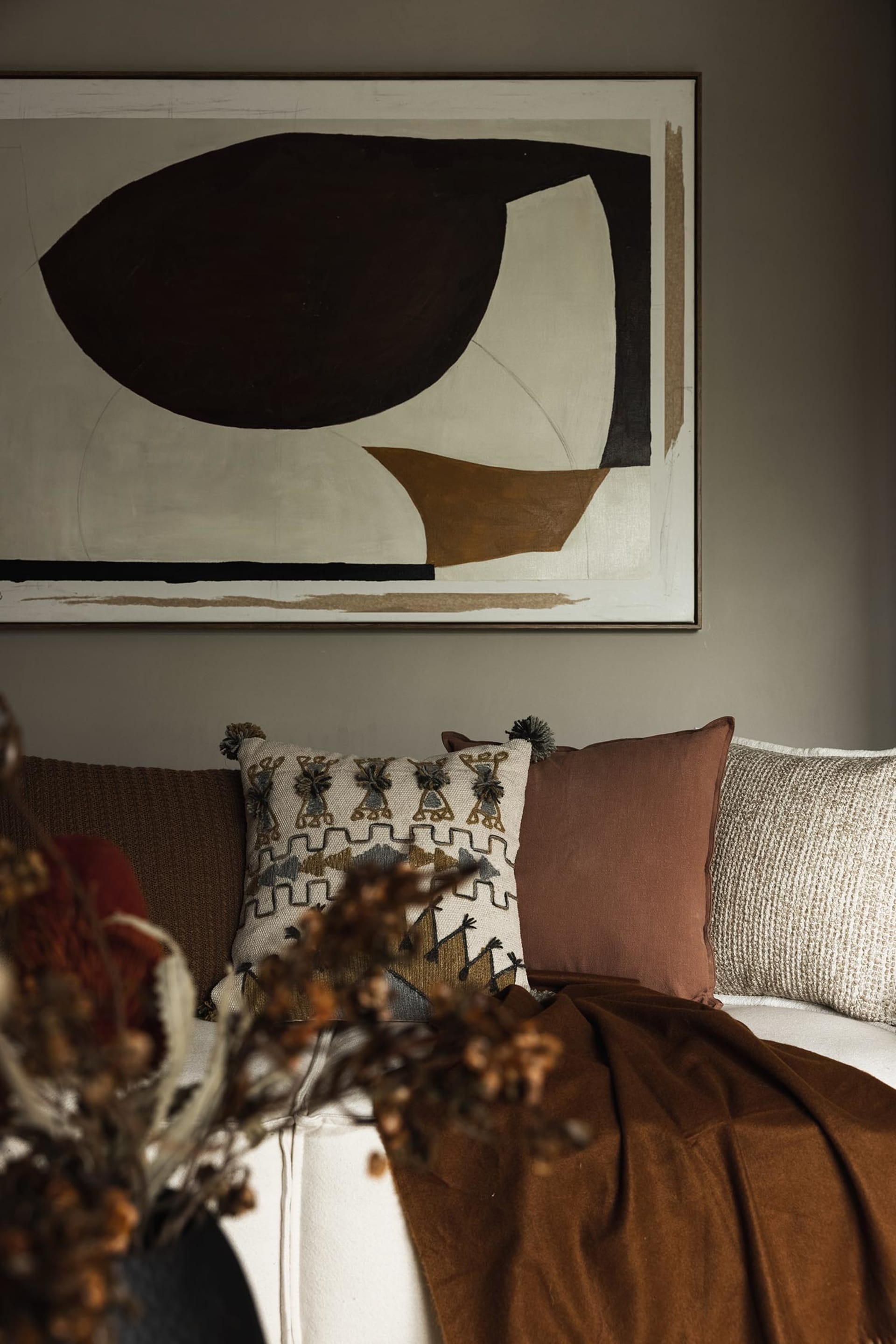 A living room with industrial-style furniture, featuring fashionable cushions in earthy tones. The scene includes a couch, pi