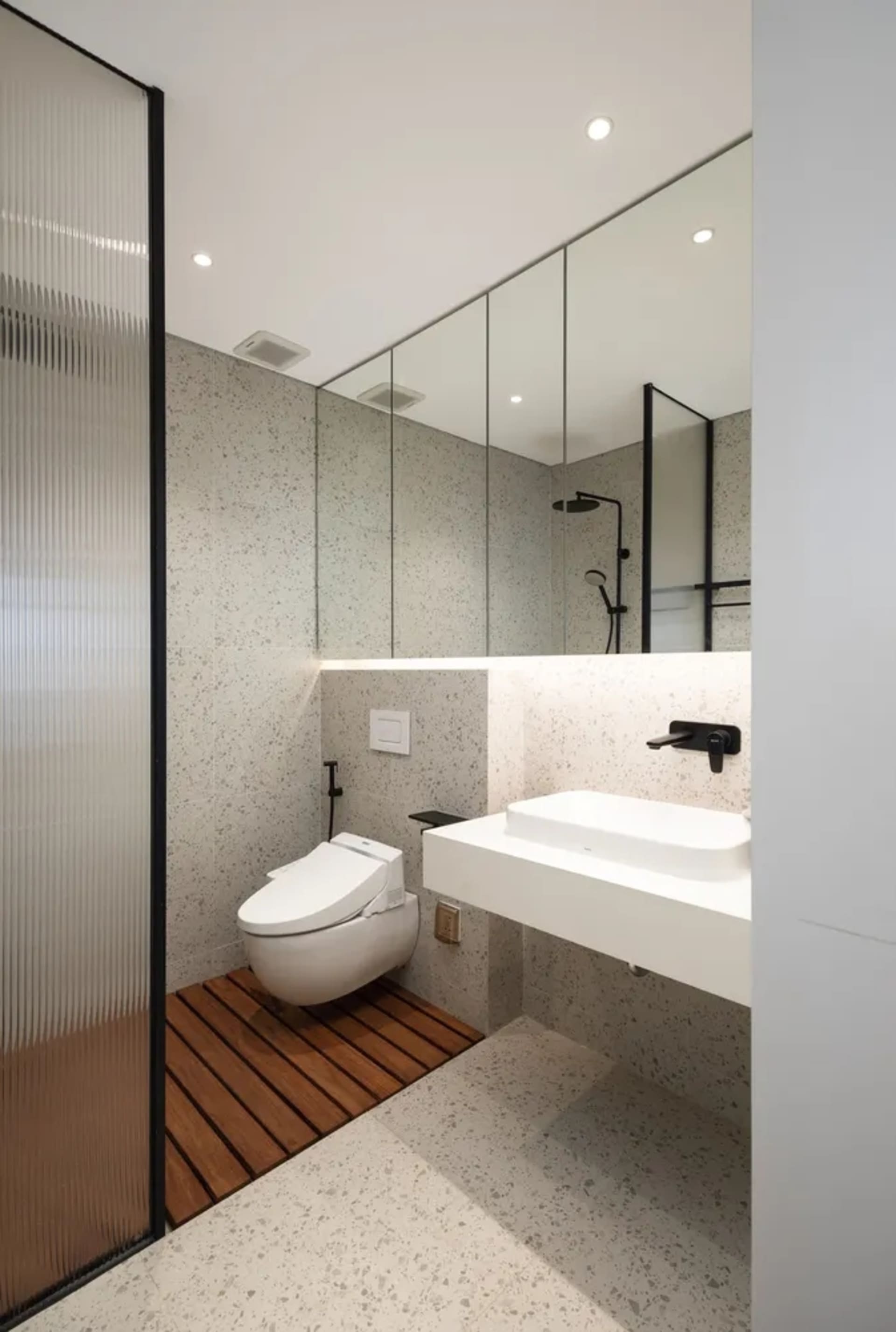 Modern minimalist bathroom with white fixtures, terrazzo floor, and large mirror.
