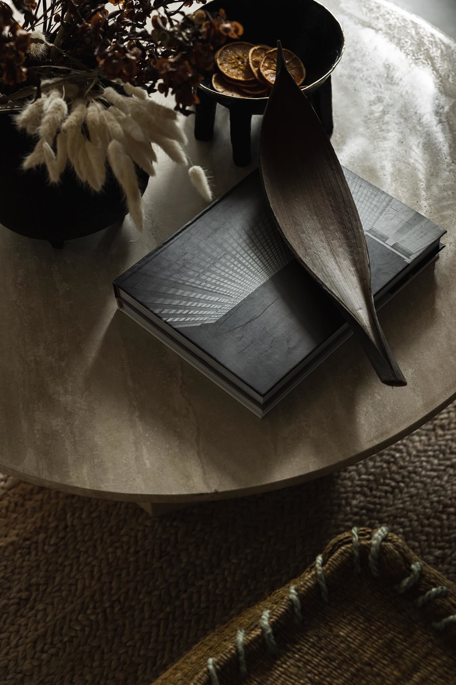 A modern coffee table decorated with a black vase containing dried flowers, a bowl of dried citrus slices, a decorative wood