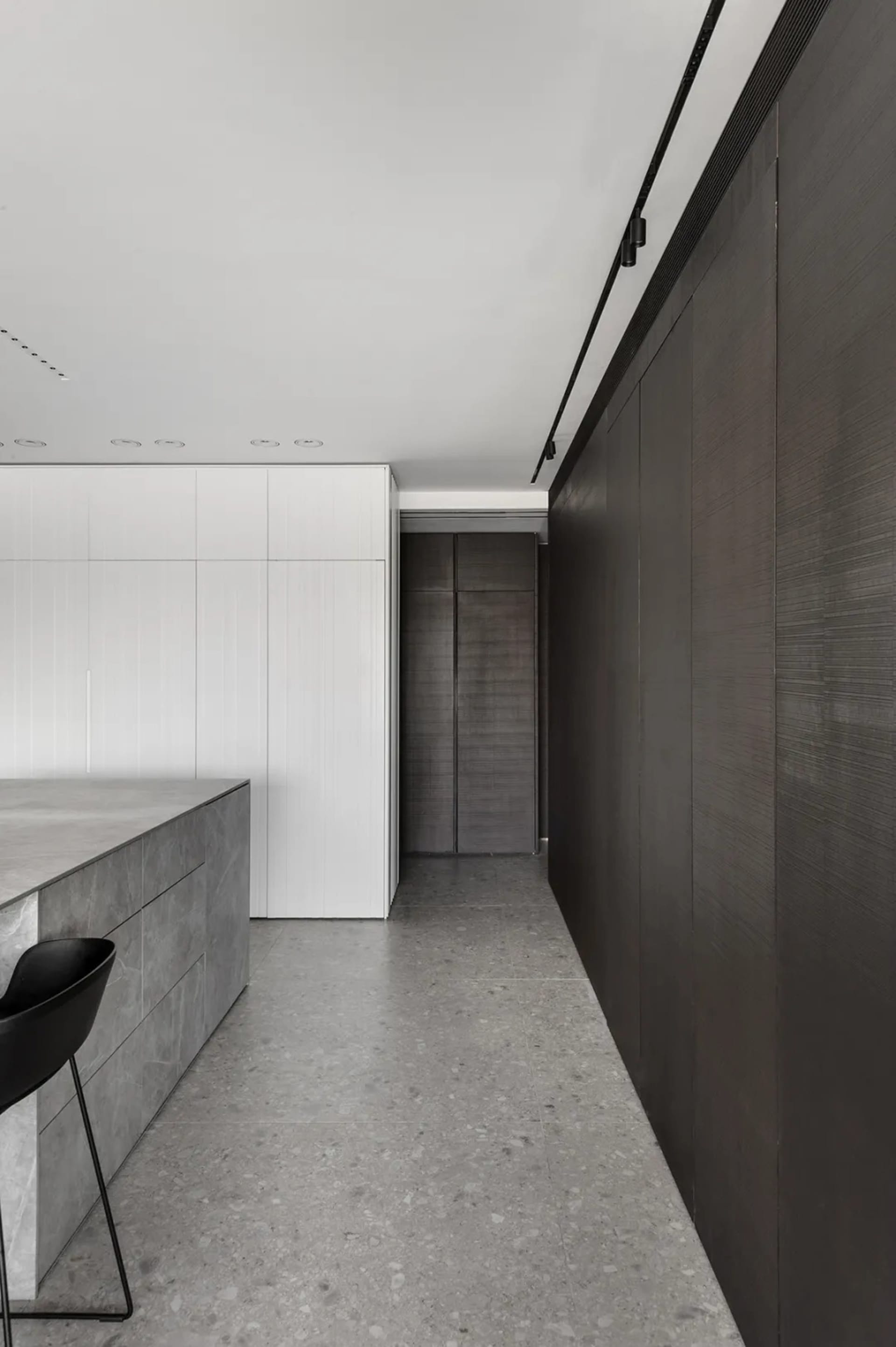A modern minimalist kitchen with a concrete countertop, white and dark wood cabinets, and black stools.