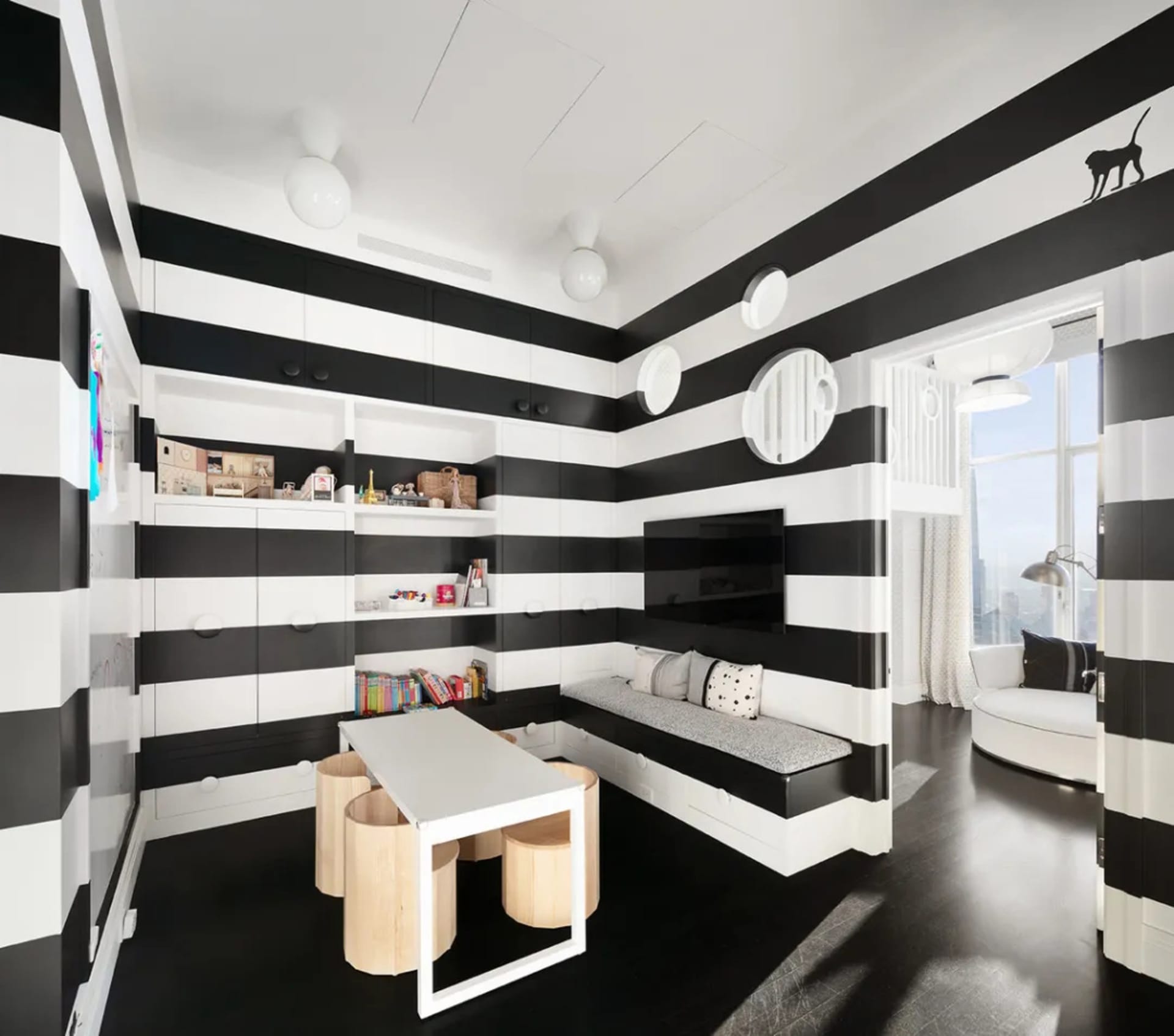 A modern minimalist child playroom featuring black and white striped walls, a built-in seating area, and a table with stools.