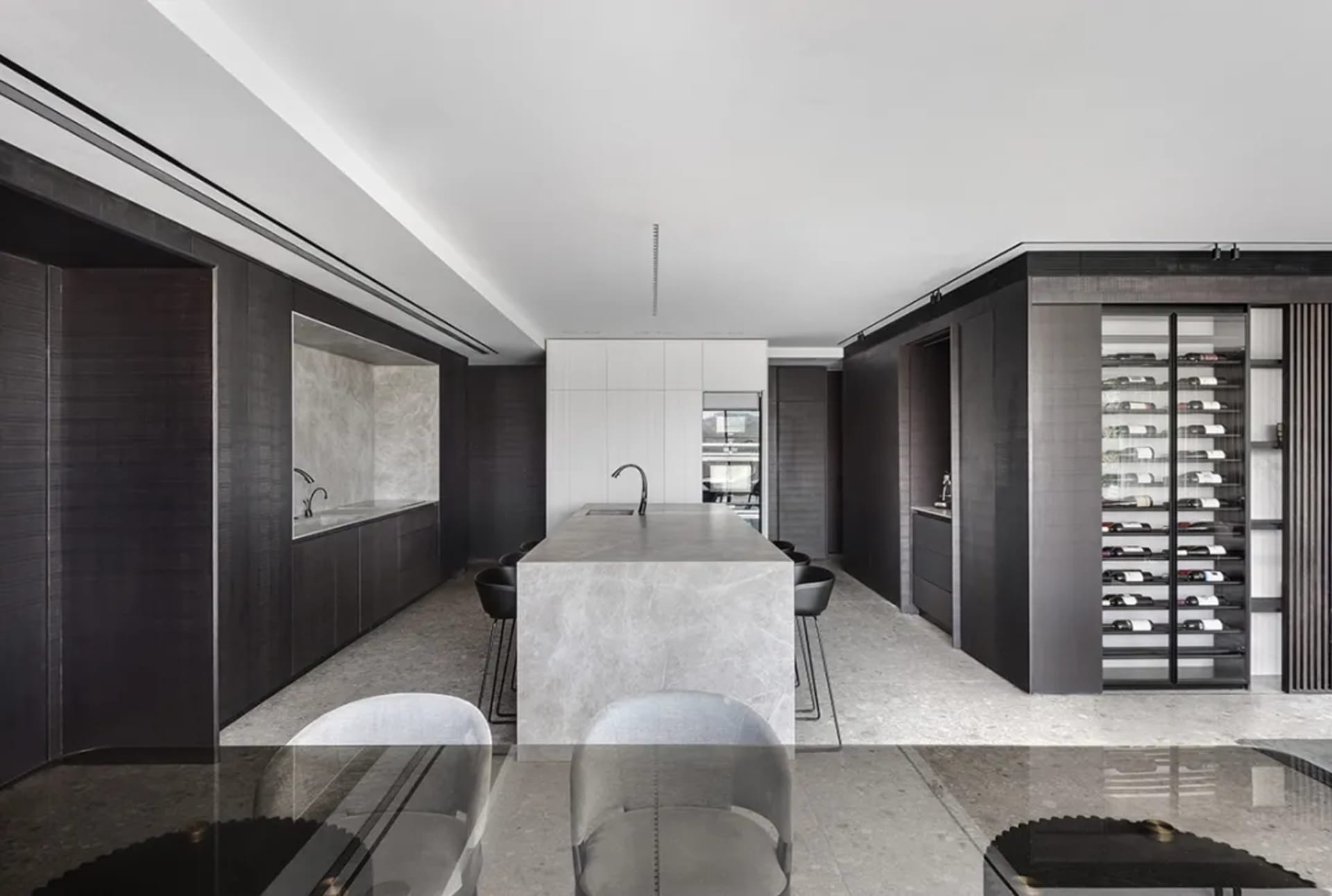 A modern residential kitchen featuring a kitchen island with a marble countertop, dark wood cabinets, and built-in wine stora