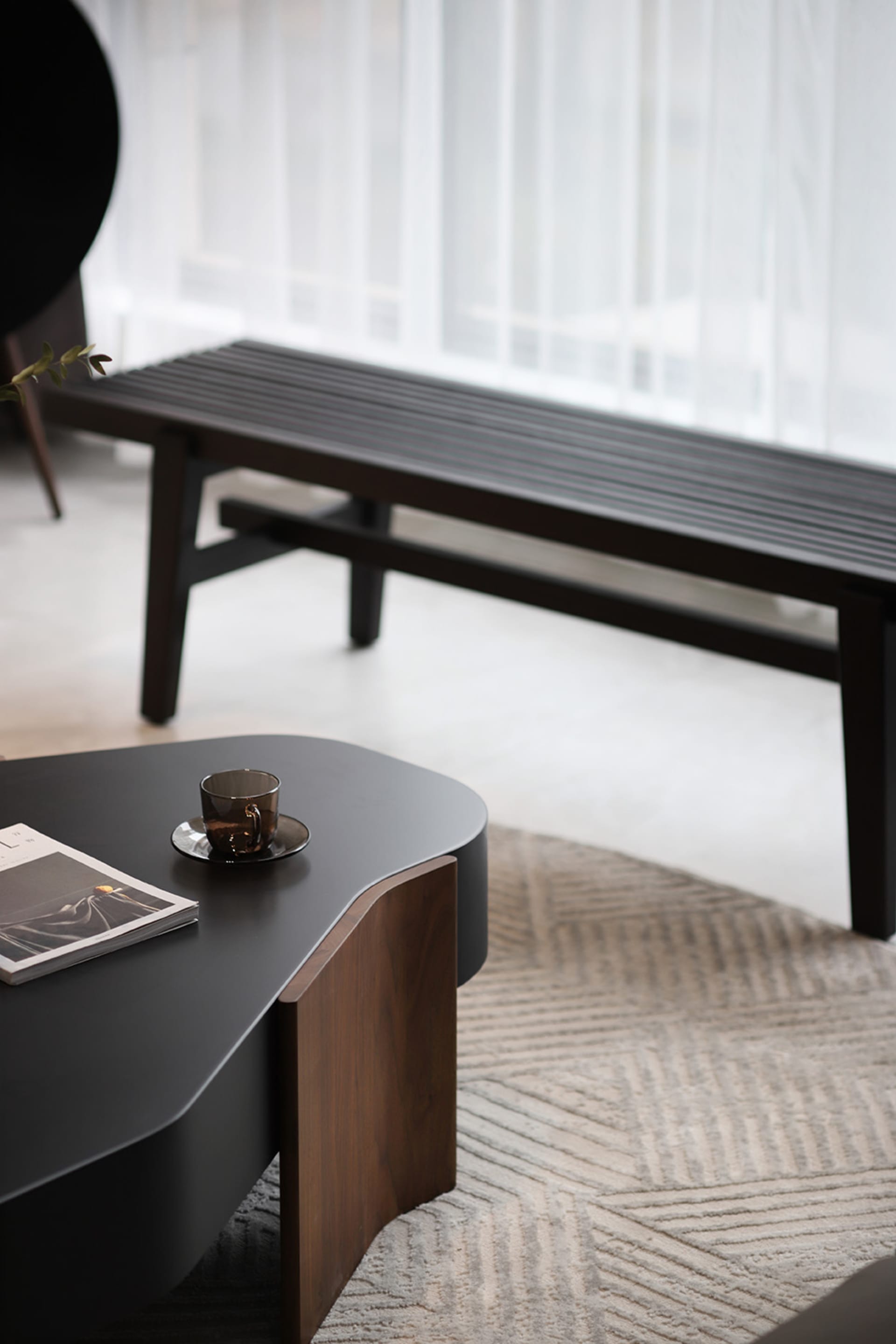 Minimalist living room with wooden table, black coffee table, and white curtains.
