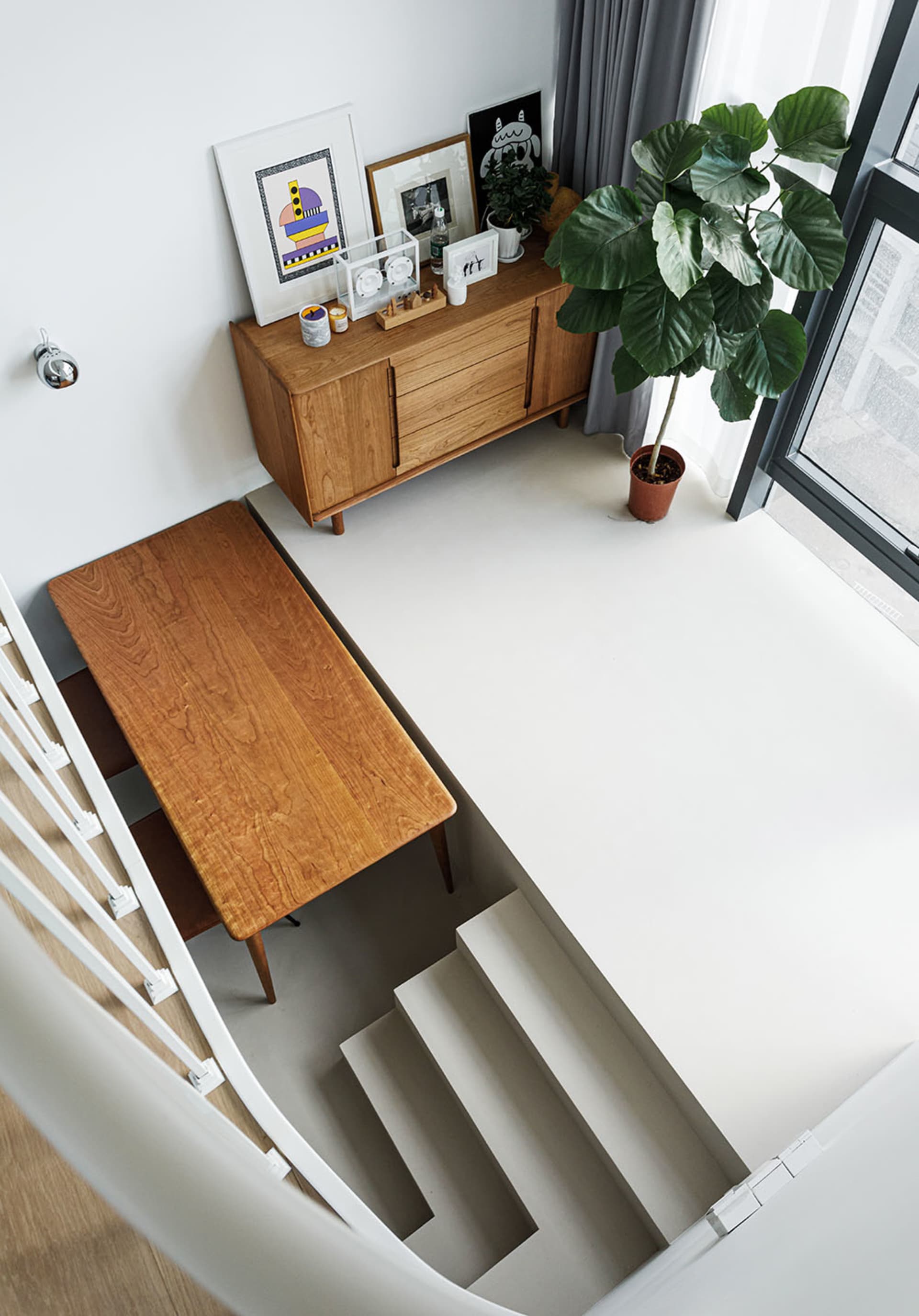 Modern minimalist interior with a wooden staircase, featuring a wooden desk, wooden cabinet, and potted plant under a large w