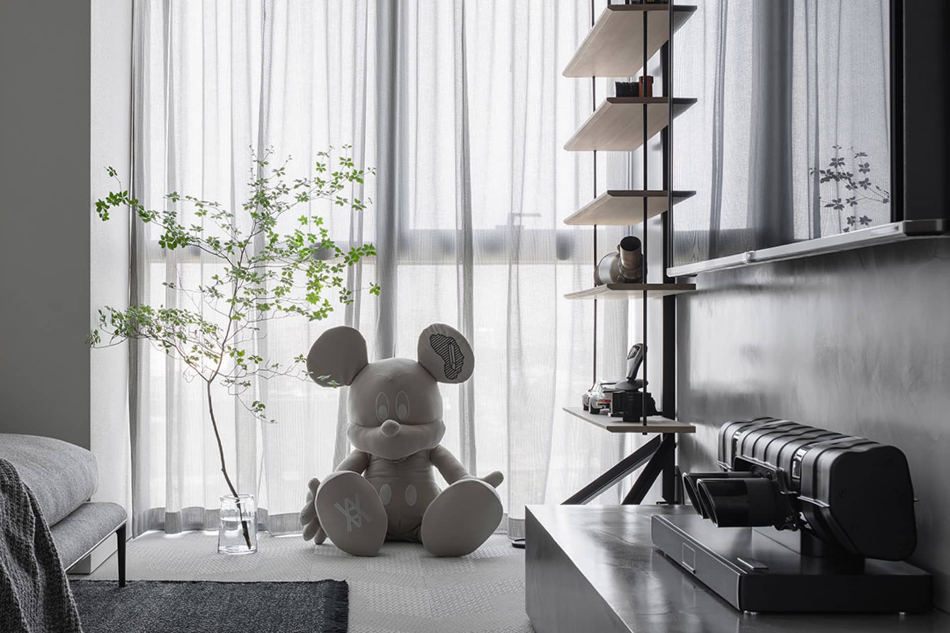A modern, urban living room featuring a plush Mickey Mouse toy, a sleek, minimalist entertainment unit with shelves, and a co