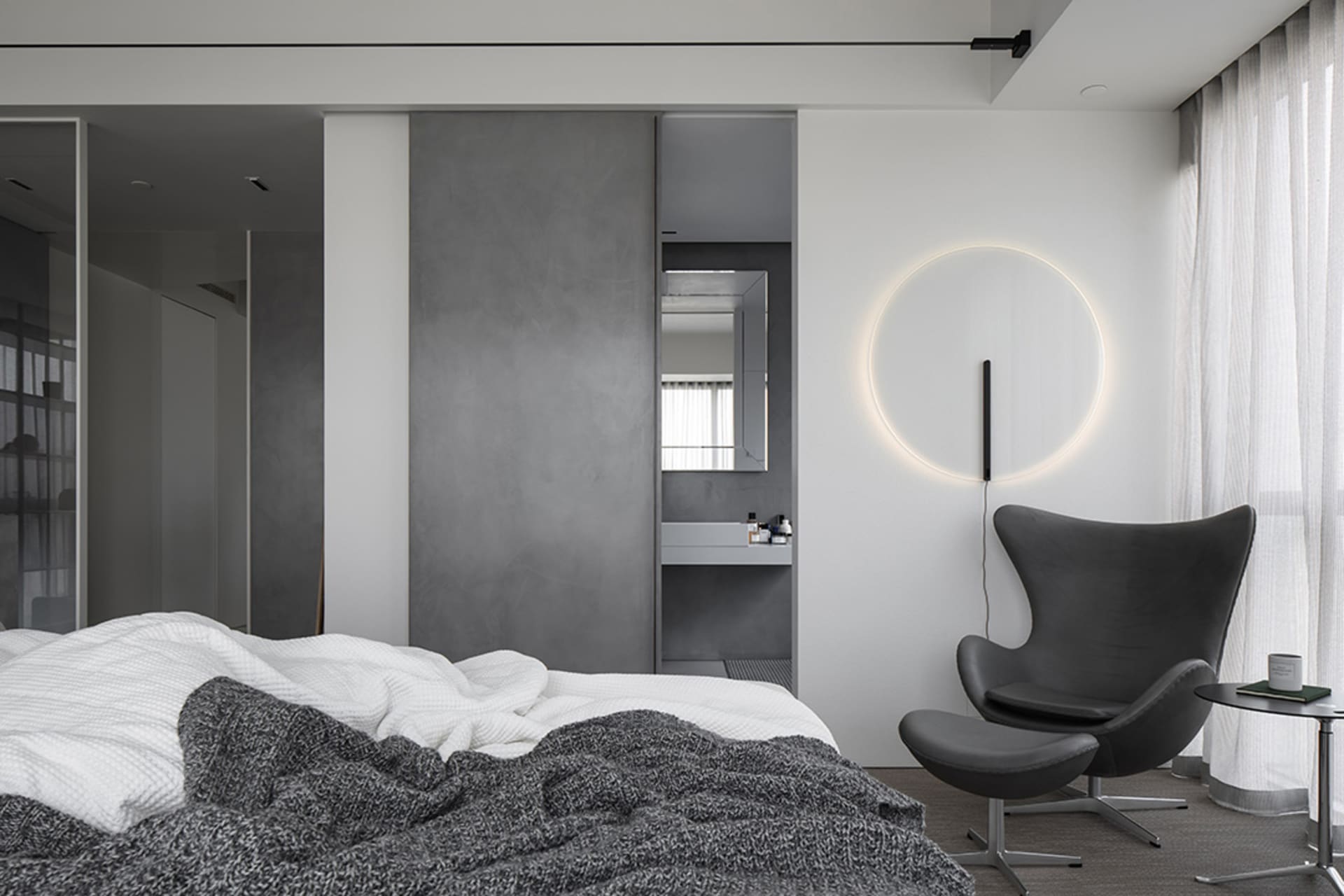 A minimalist bedroom featuring a concrete wall and a circular light fixture.