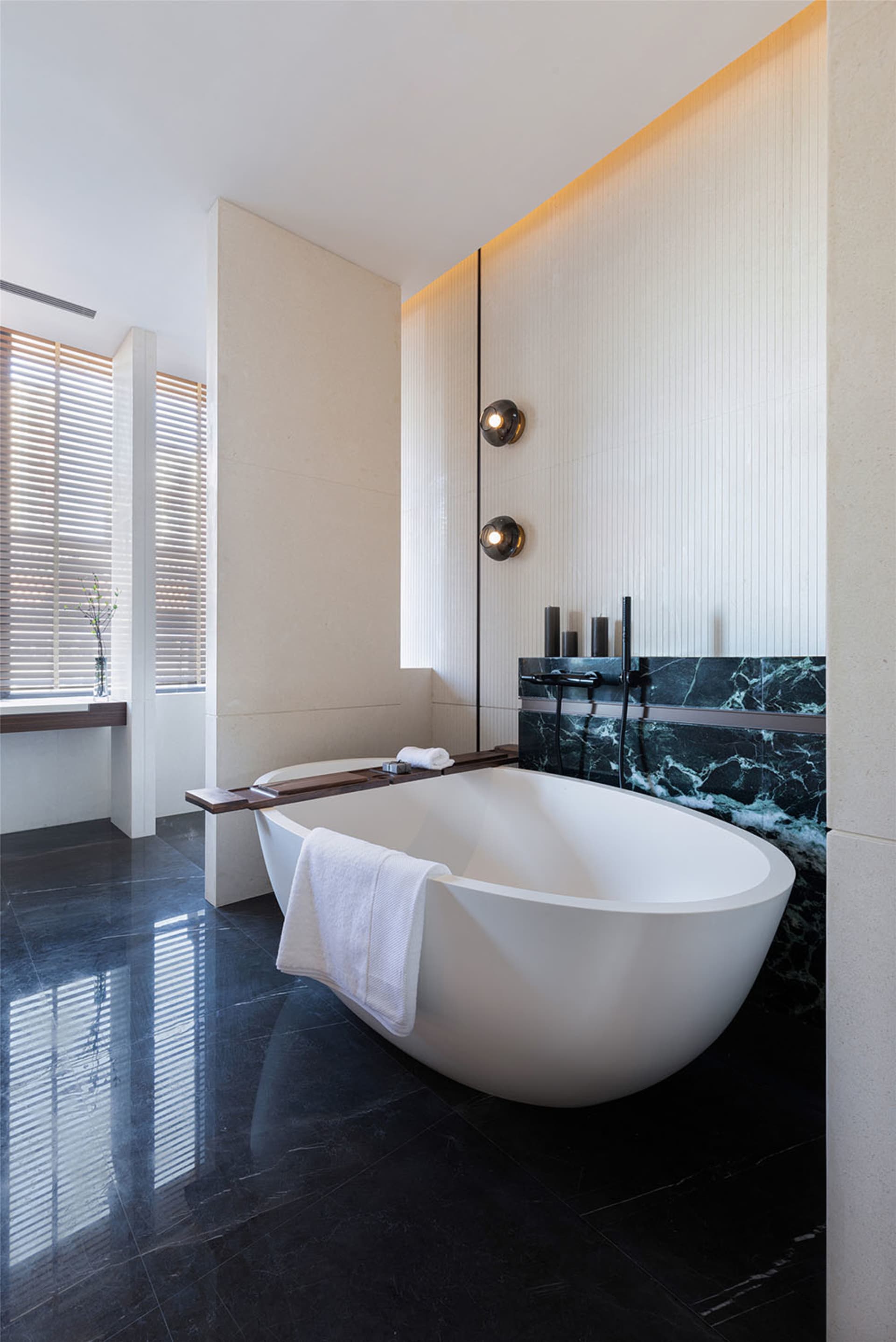 Modern minimalist bathroom featuring a white freestanding bathtub on a black marble floor, with a window allowing natural lig