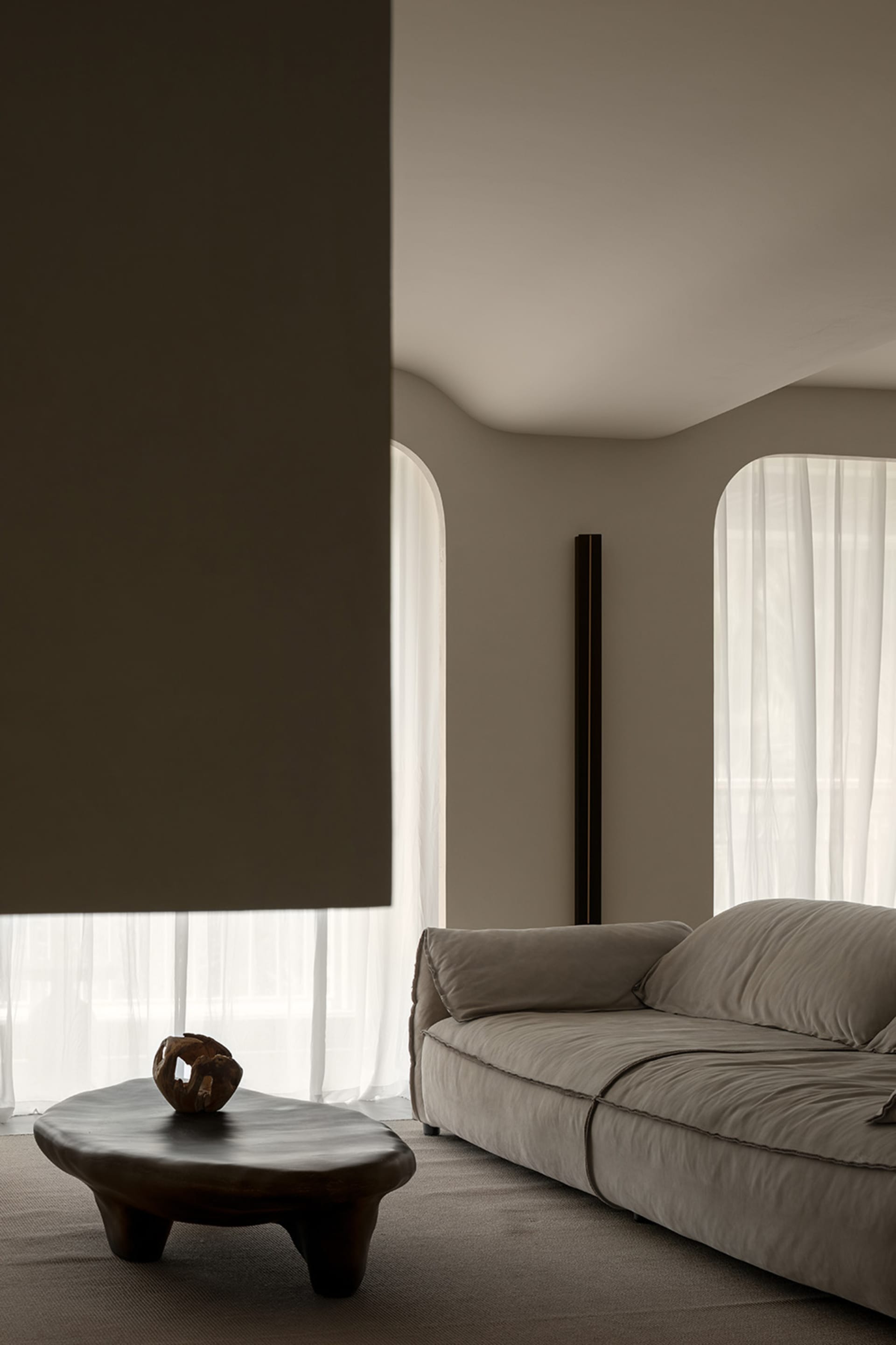 A minimalist living room featuring a fabric coffee table with a unique wooden sculpture on top, and a comfortable sofa.