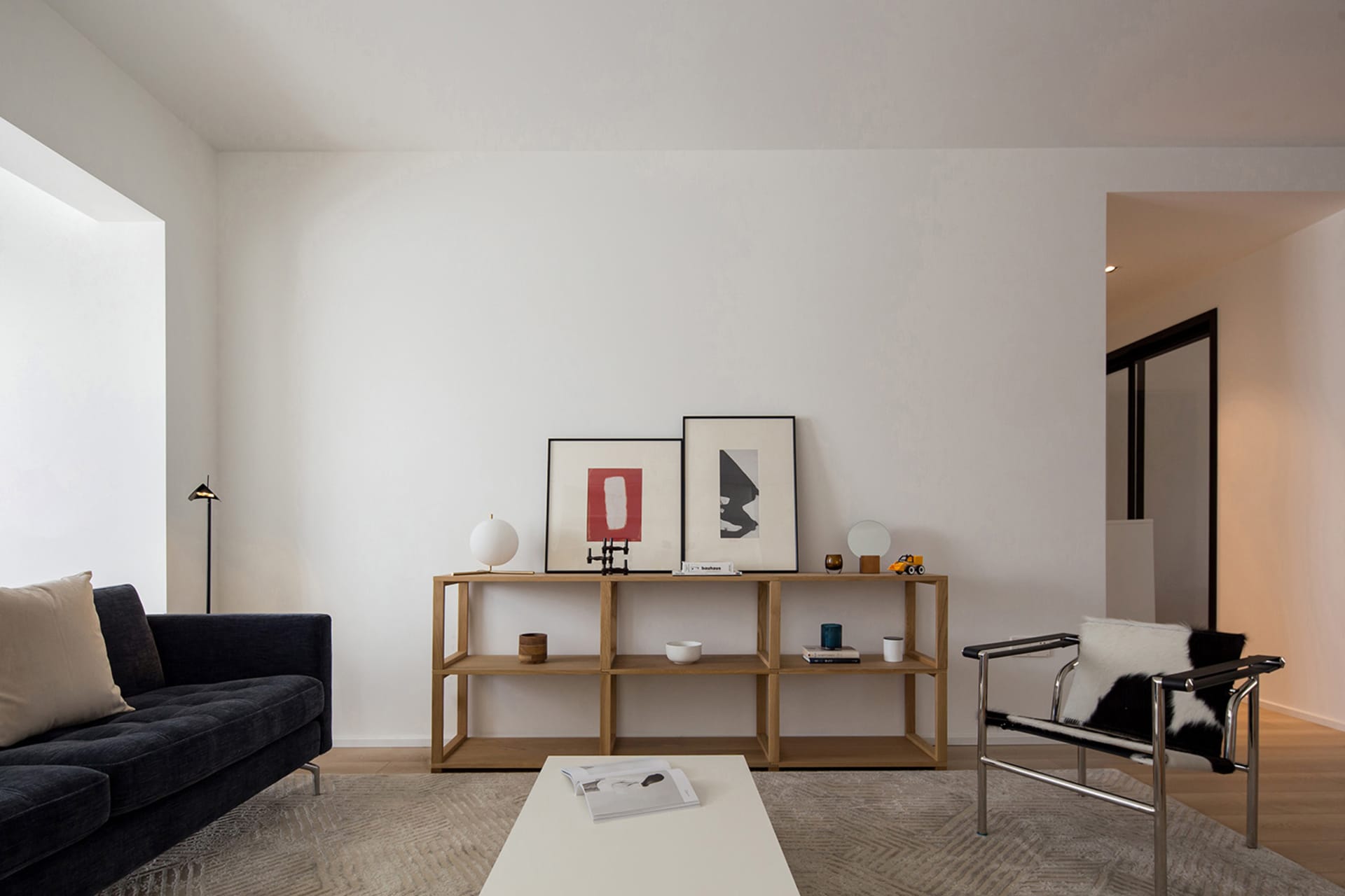 A minimalist living room featuring wooden shelves and a black sofa with white cushions.