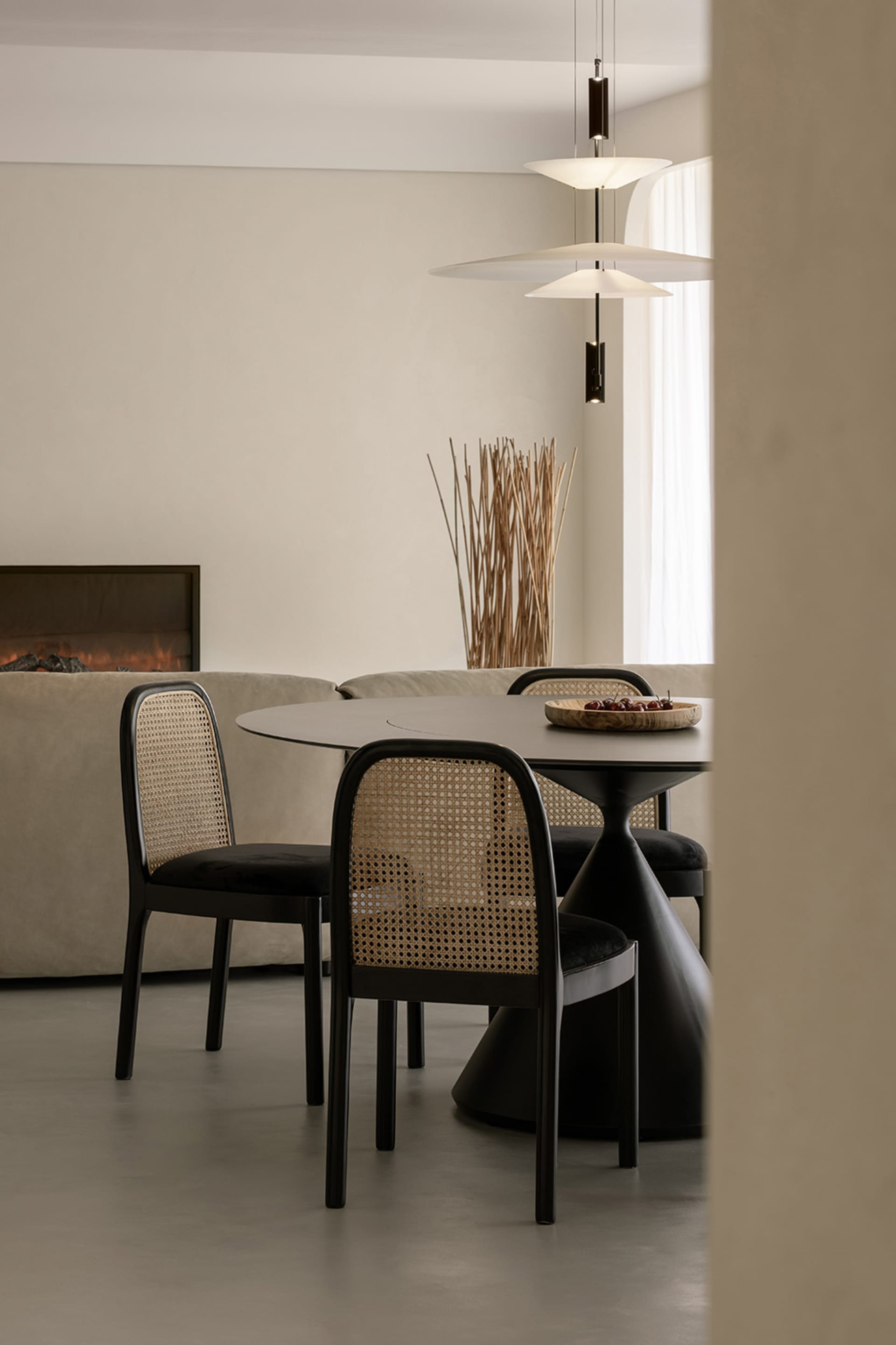A modern minimalist dining area with a round table, wicker chairs, and a fireplace.