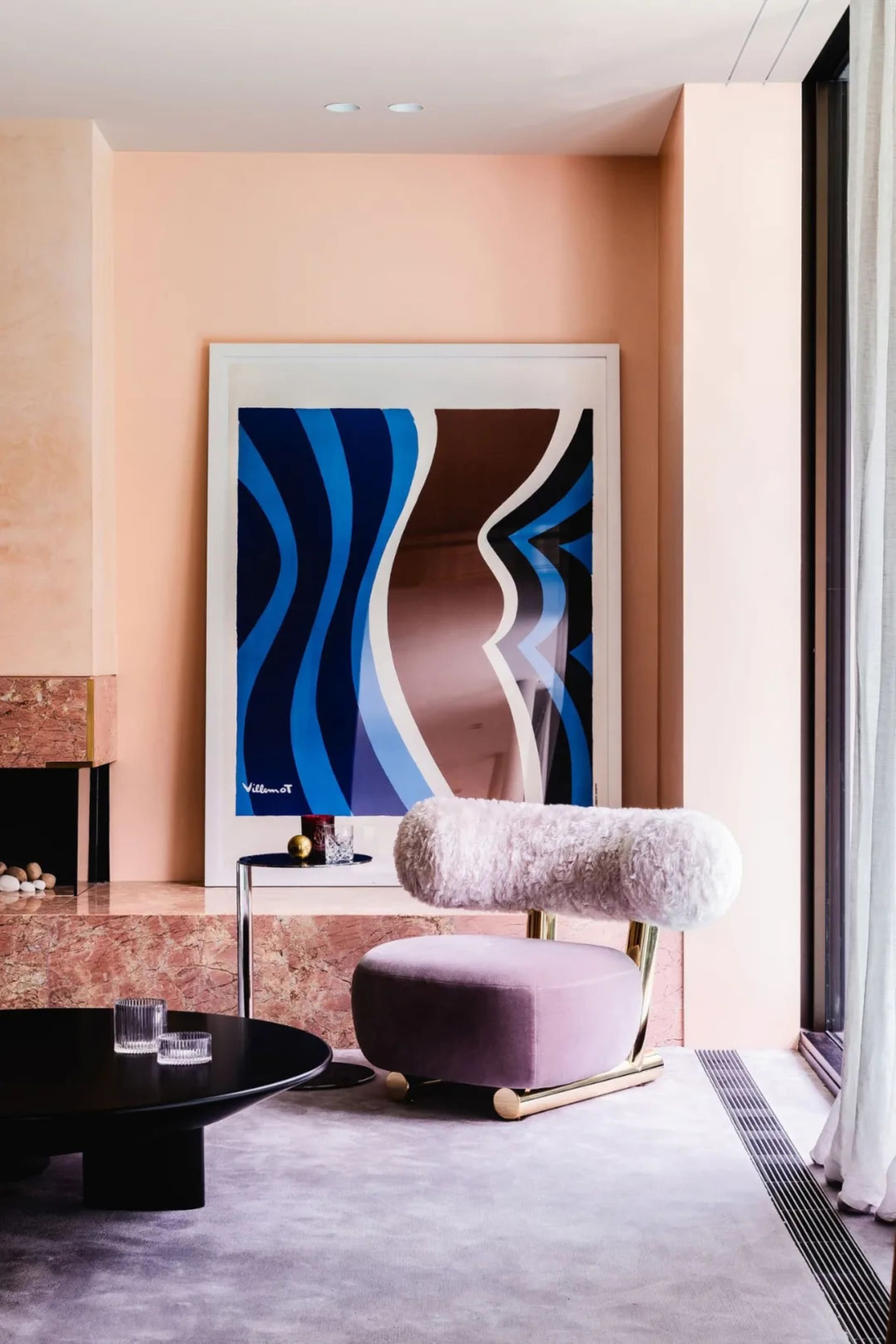A modern living room with a marble fireplace, plush armchair, and abstract art hanging on the wall