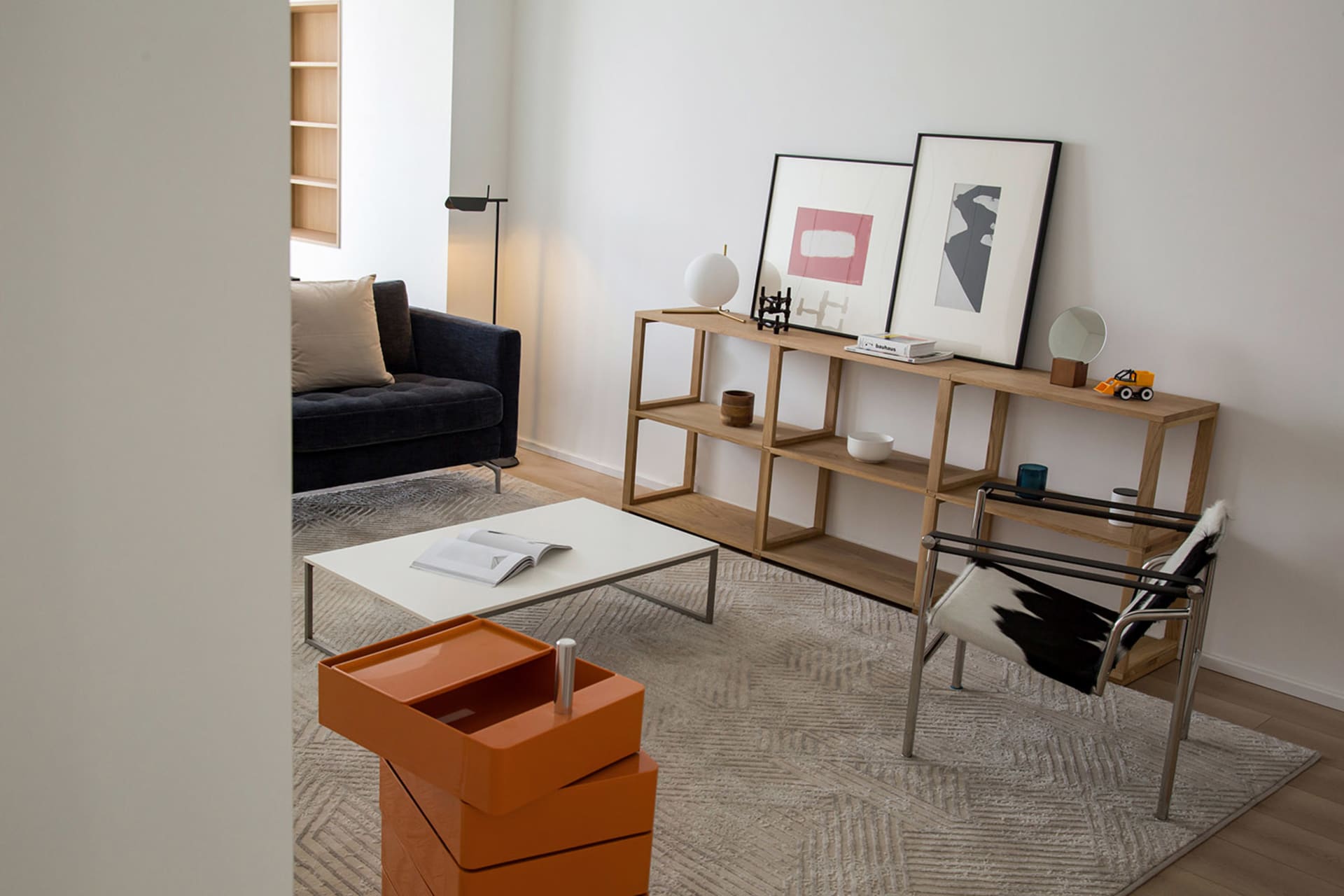 Modern minimalist living room with a black sofa, white coffee table, and wooden shelving unit.